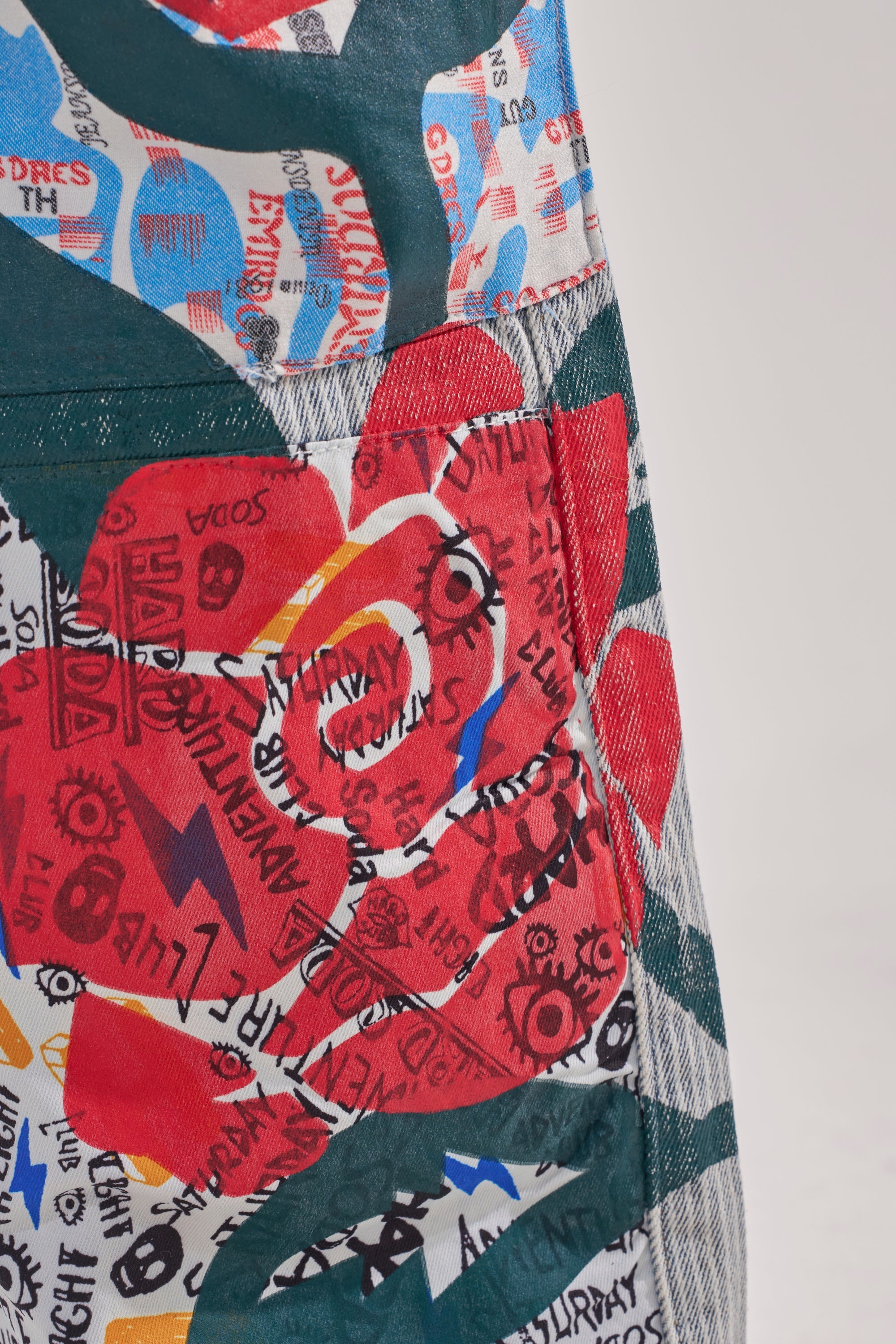 A close-up of fabric with bold red roses, vibrant text, symbols, and abstract patterns on a white and green background—perfect for styling with the CIAO BELLA STRIPE TROUSER. 9