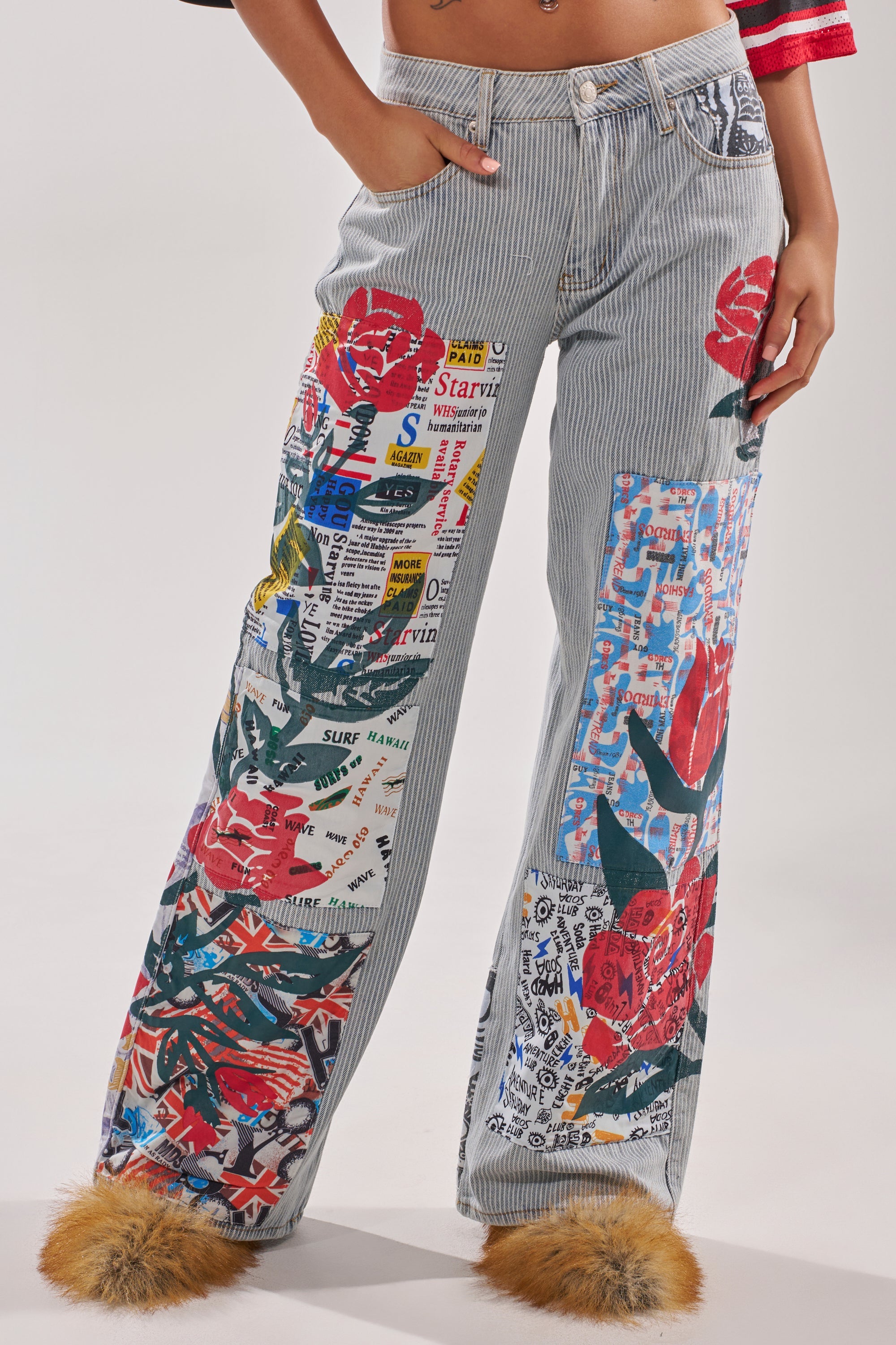 Wearing the CIAO BELLA STRIPE TROUSER—light blue striped denim wide-leg pants with colorful patches and furry ankle cuffs—a person casually rests a hand in one pocket. 1