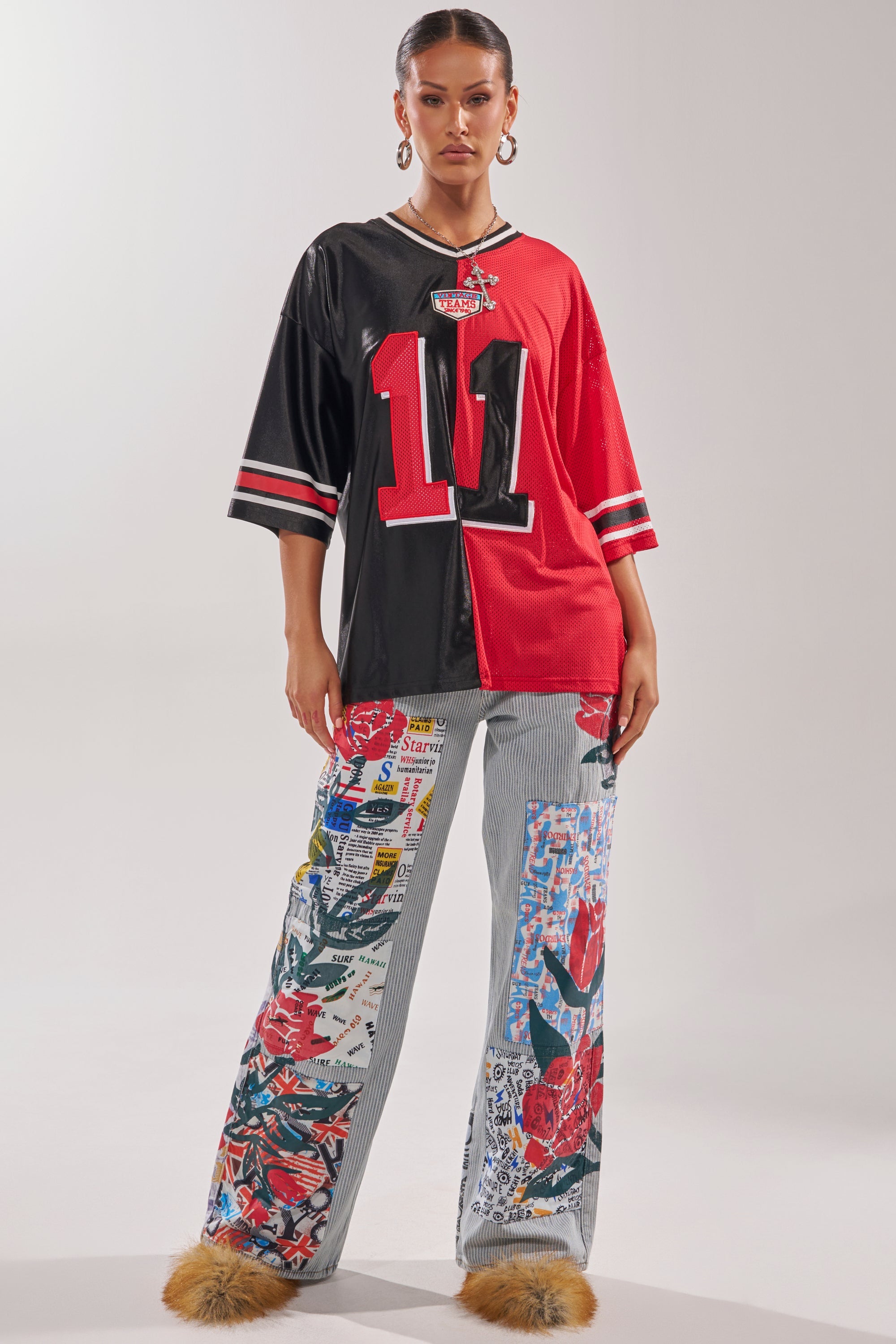 A woman stands against a plain white background wearing a split black and red football jersey with the number 11, CIAO BELLA STRIPE TROUSER featuring patchwork denim with floral and graphic prints, and brown furry shoes. 5