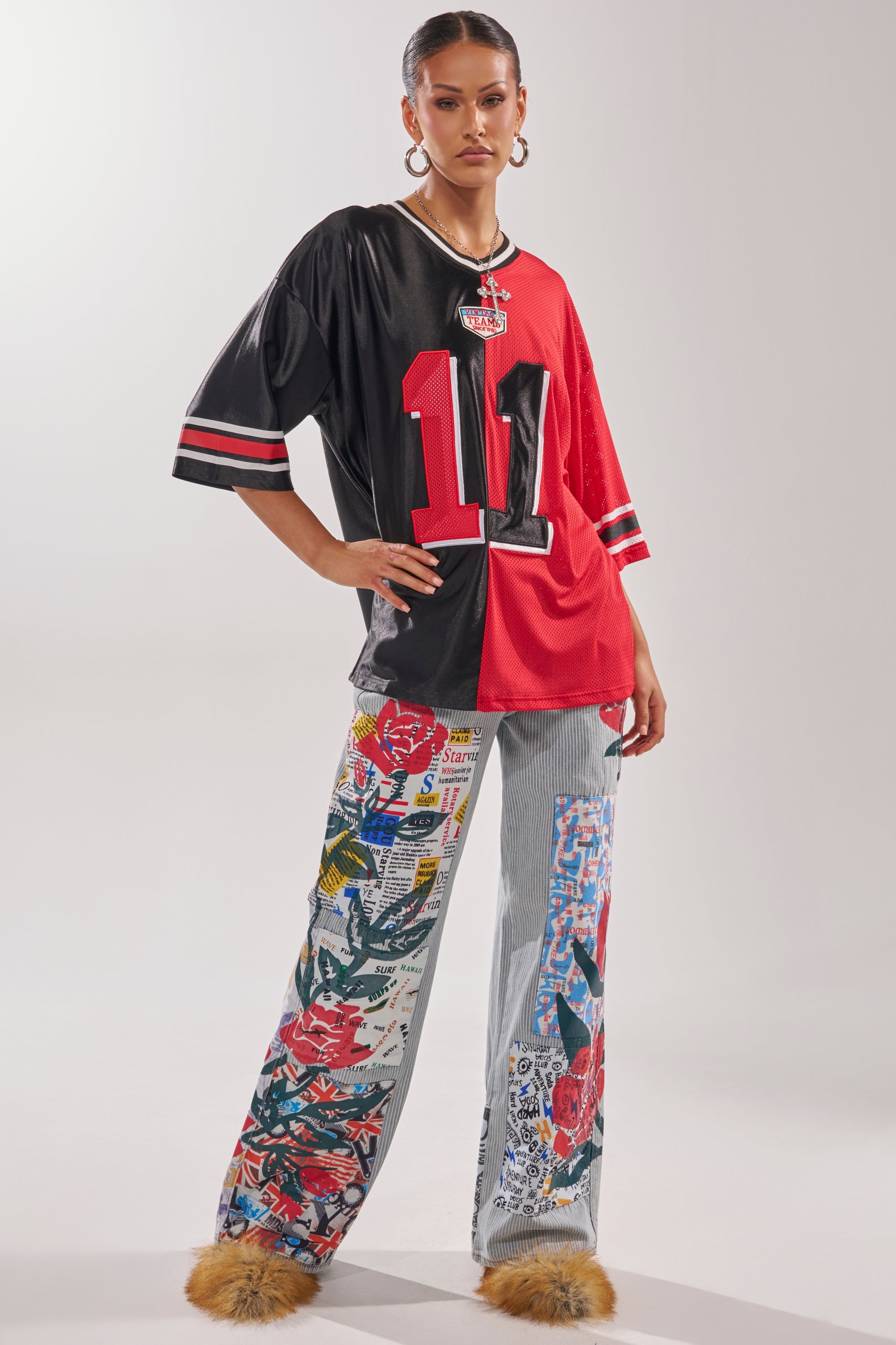 A woman stands confidently in CIAO BELLA STRIPE TROUSER, a split-color football jersey with number 11, large hoop earrings, and tan furry shoes against a plain backdrop. 6