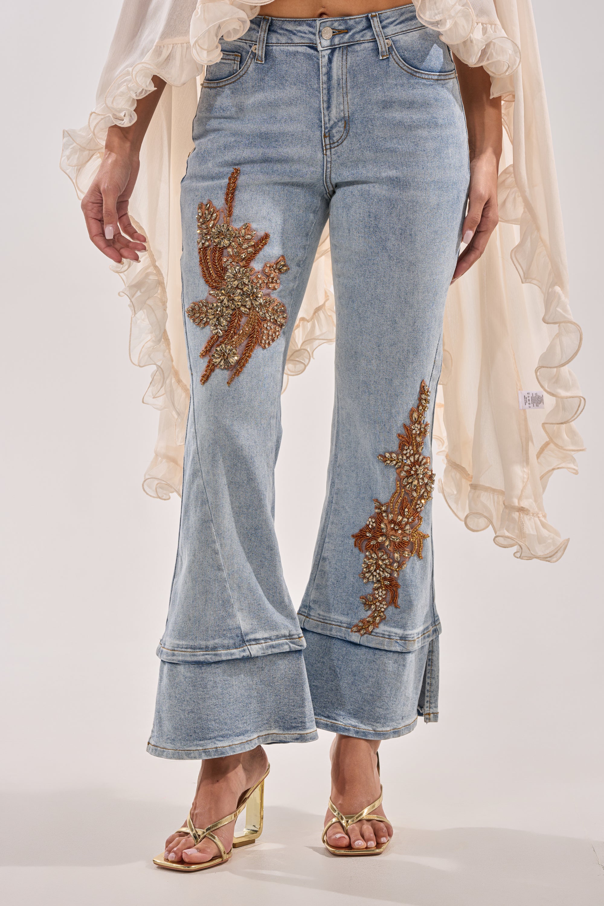 Someone in TOTALLY COOL RELAXED DENIM featuring gold beaded embroidery on both legs, styled with gold sandals and a sheer, ruffled cream top. 0