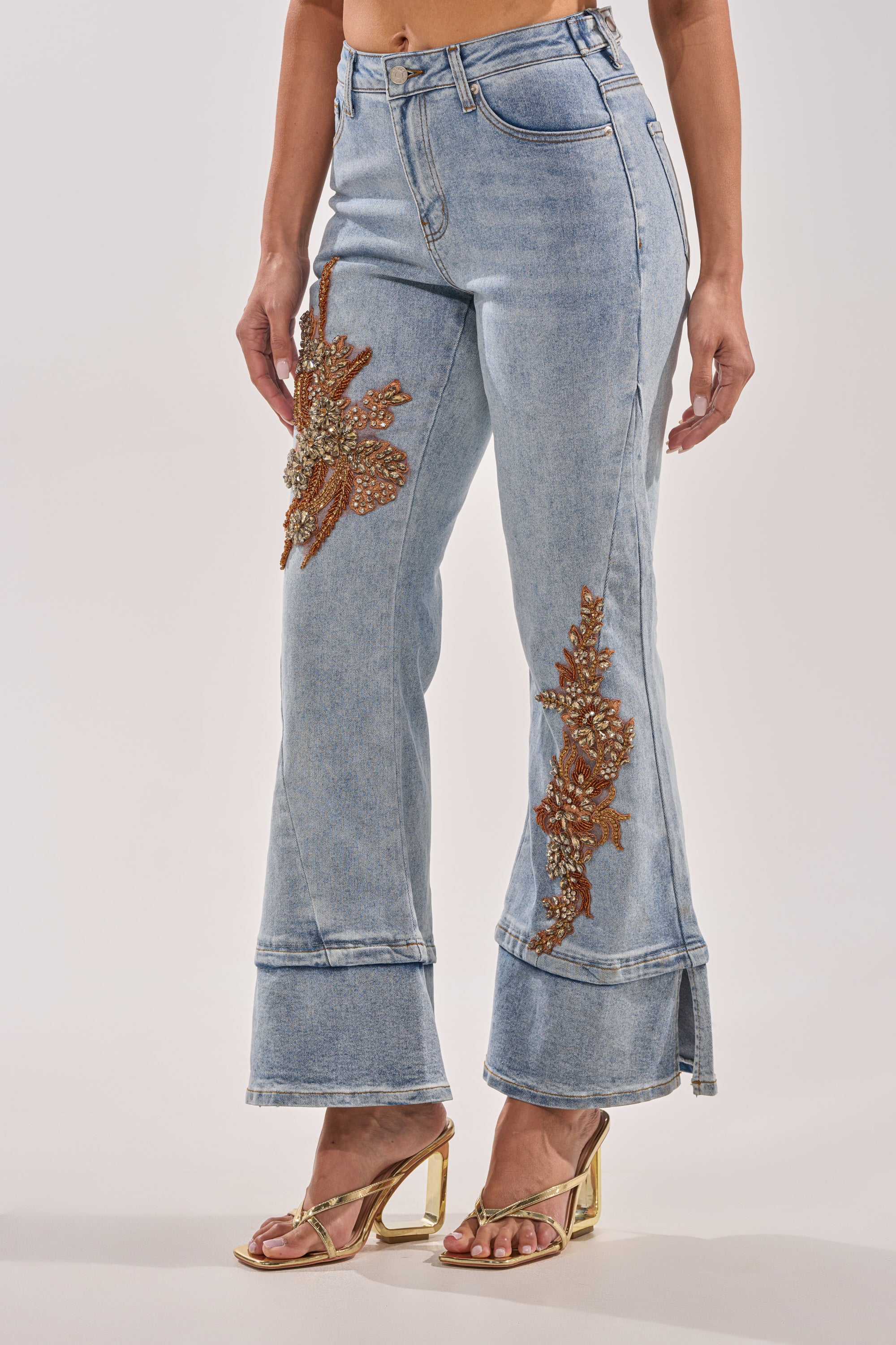 A person wearing TOTALLY COOL RELAXED DENIM pants with flared hems and brown and gold floral bead embroidery, styled with gold open-toe high-heeled sandals. 1