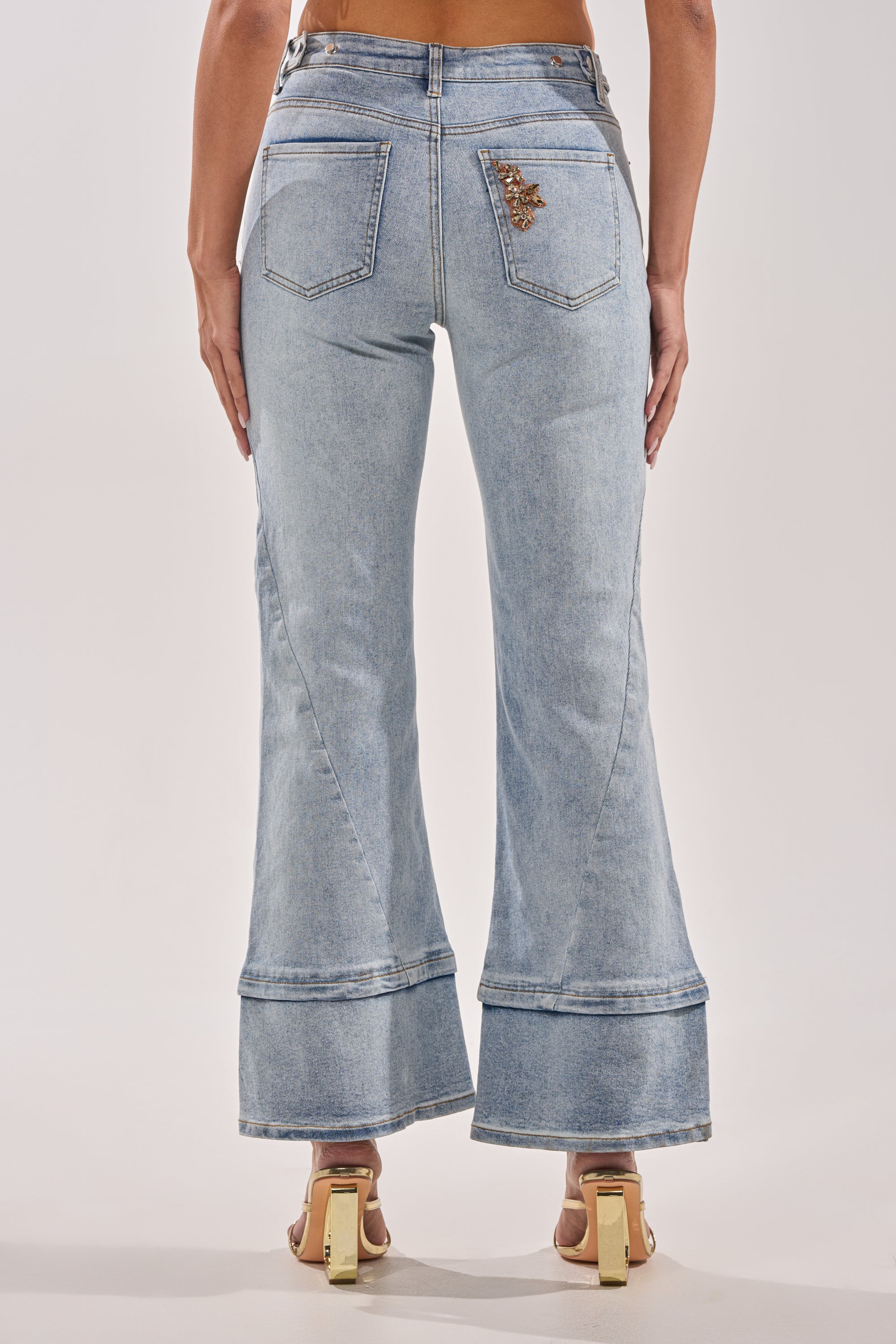 A person wearing TOTALLY COOL RELAXED DENIM with decorative stitching, two back pockets, layered hems, and a metallic detail on one pocket stands facing away from the camera. 2