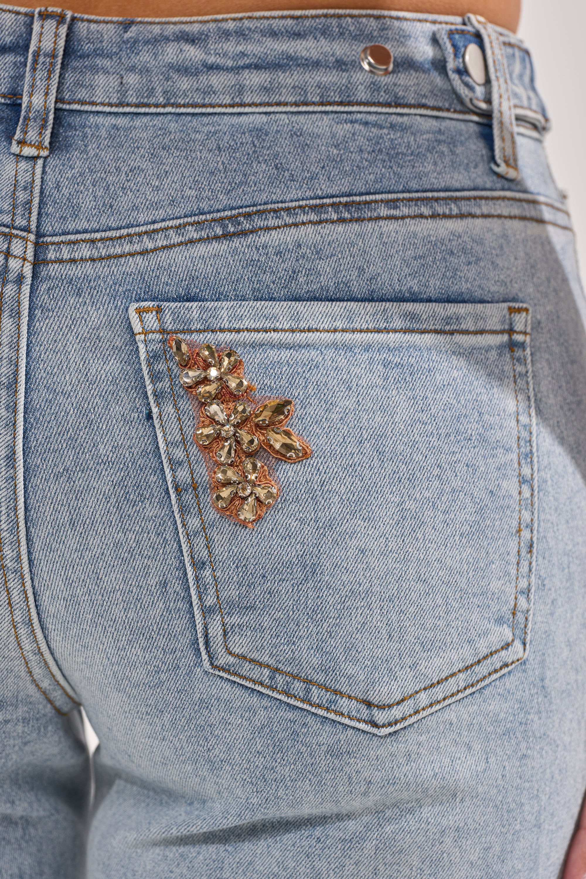 Close-up of the back pocket on TOTALLY COOL RELAXED DENIM in light blue, showcasing a decorative floral design embellished with gold and crystals. 5