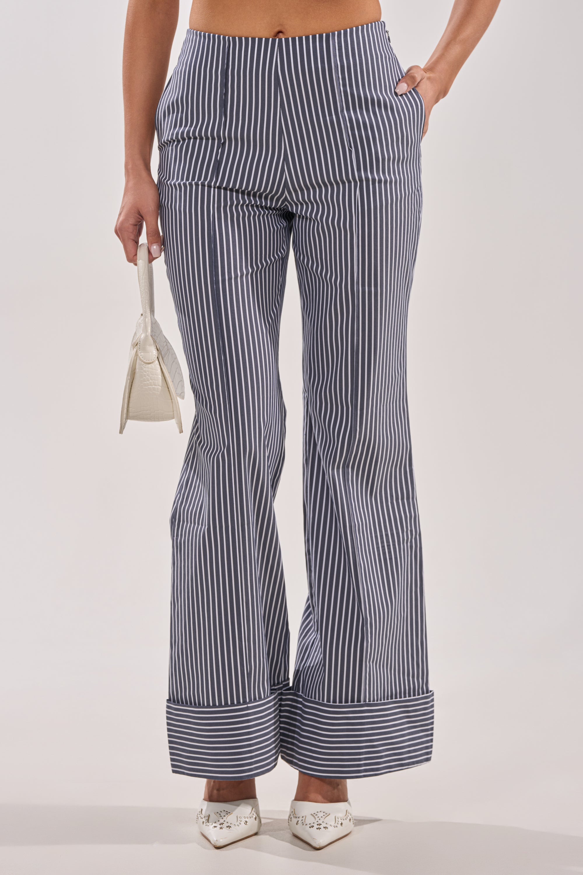 Wearing the MISS POPULAR POPLIN TROUSER—navy and white wide-leg pinstripe pants with a large cuff—paired with a small white handbag and white pointed flats. 1