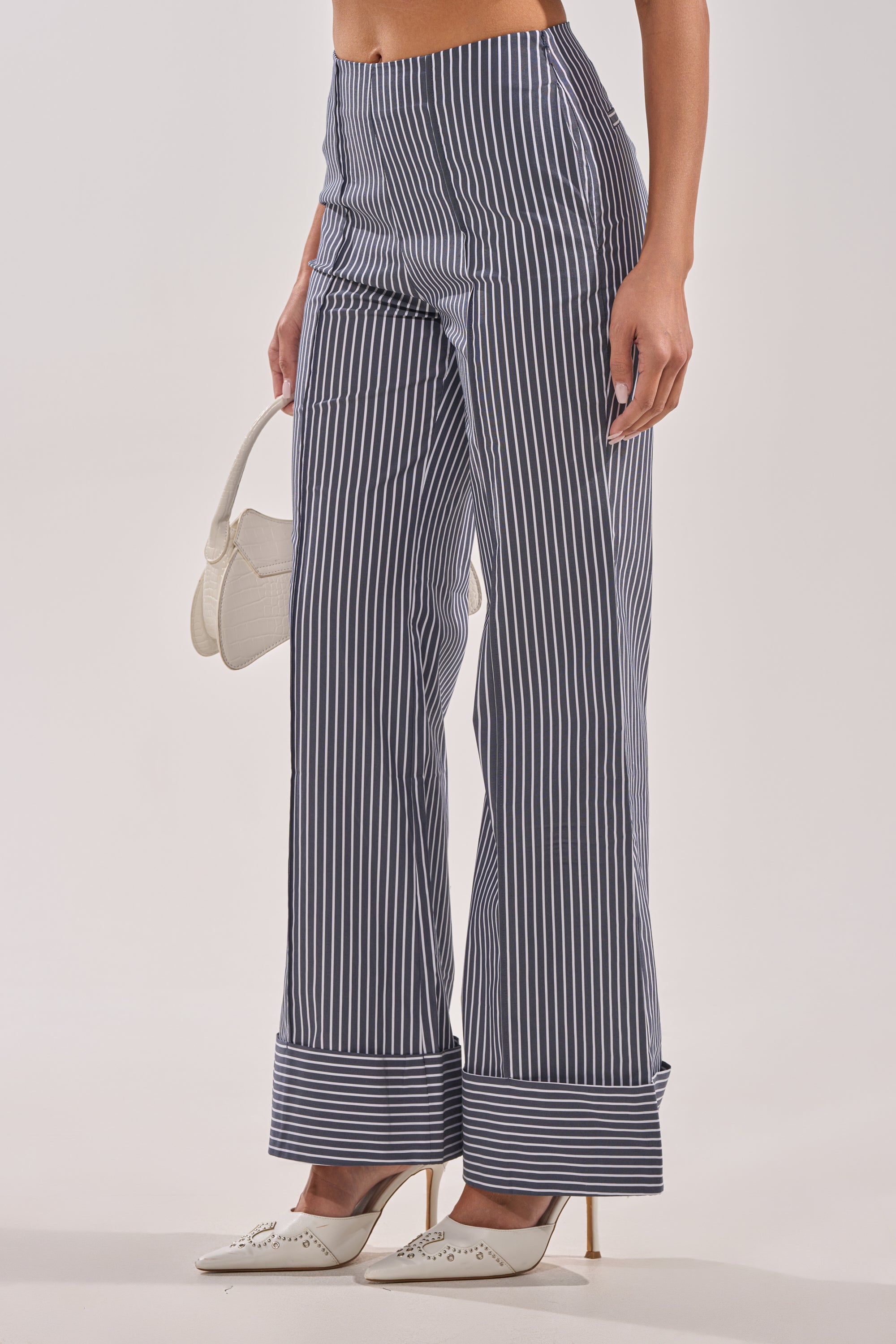 A woman is shown from the waist down wearing MISS POPULAR POPLIN TROUSER wide-leg pinstripe pants with a high-rise waist, styled with white pointed heels and a chic white handbag. 3