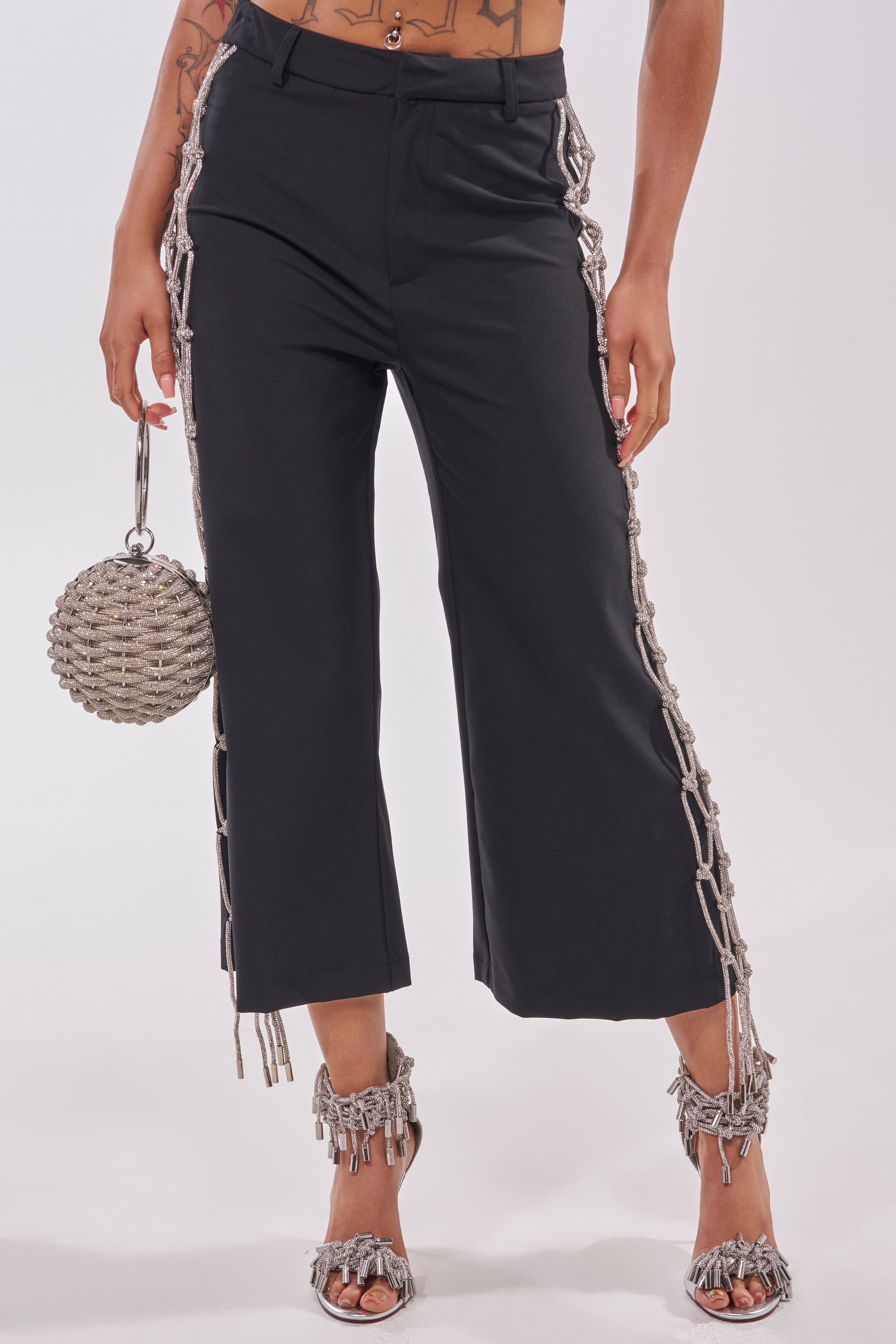 A person wearing NINA RHINESTONE CULOTTES—sequin wide-leg pants with silver chain fringe on the sides—silver fringe sandals, and holding a round silver beaded handbag. Only their lower half is shown. 2