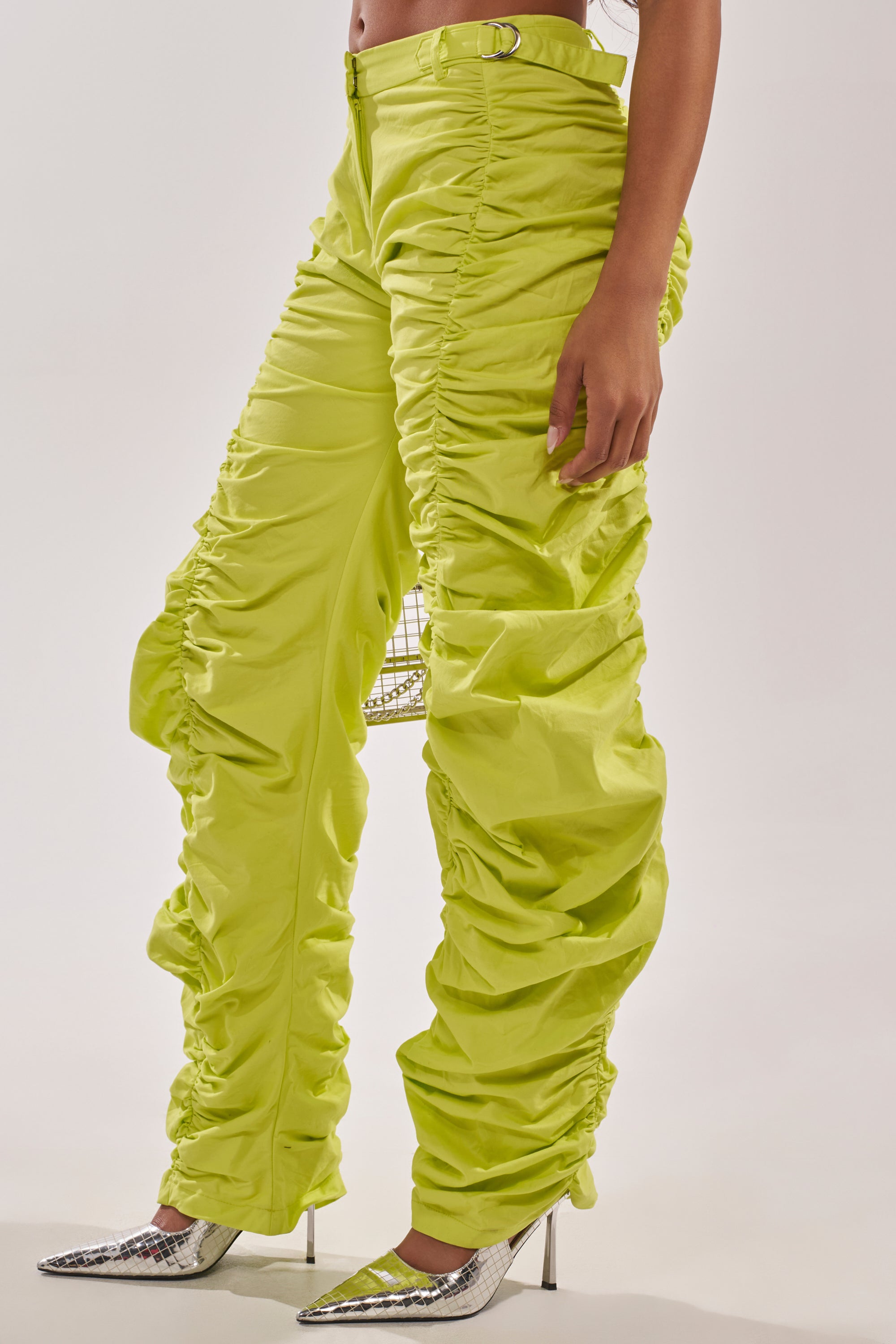 A person stands against a plain white background in the NOT IN THE MOOD RUCHED TROUSER—green, high-rise, and festival-ready—styled with silver pointed-toe heels for a bold statement look. 2