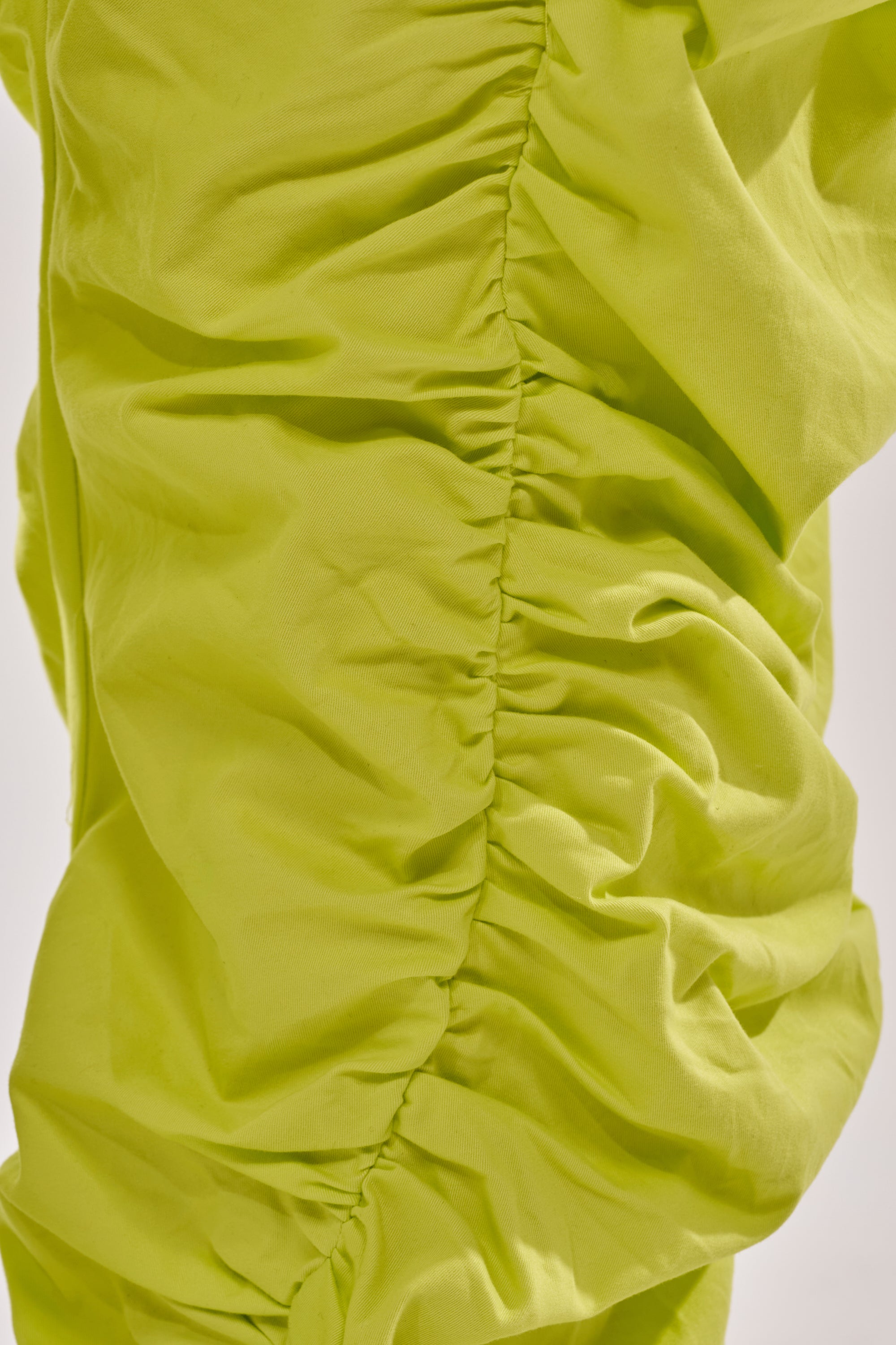 Close-up of bright lime green ruched fabric with gathered, wrinkled texture and vertical seams—a striking detail featured on the NOT IN THE MOOD RUCHED TROUSER. 5