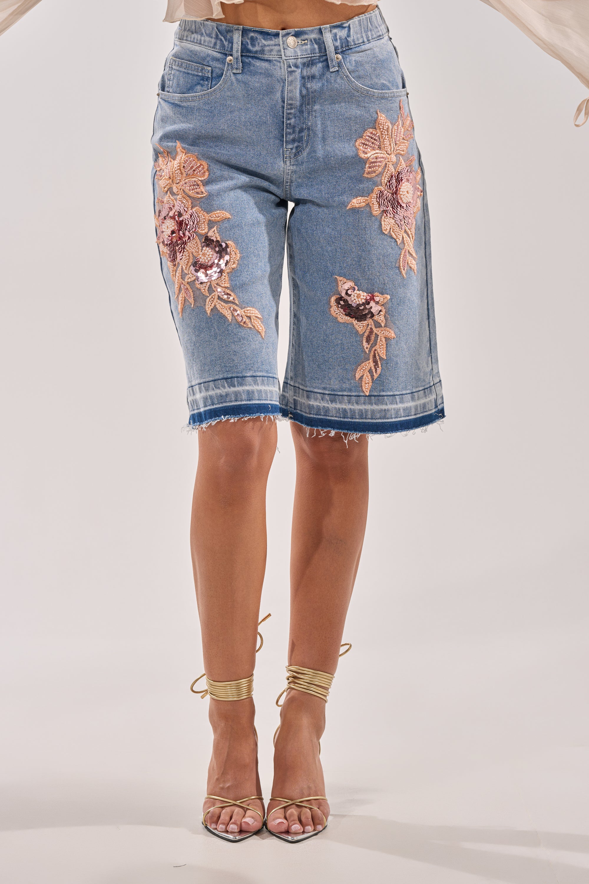 A person wearing TRY ME DENIM BERMUDA SHORTS with high-rise fit, frayed hems, and bold floral embroidery on the front, styled with strappy high-heeled sandals. 1