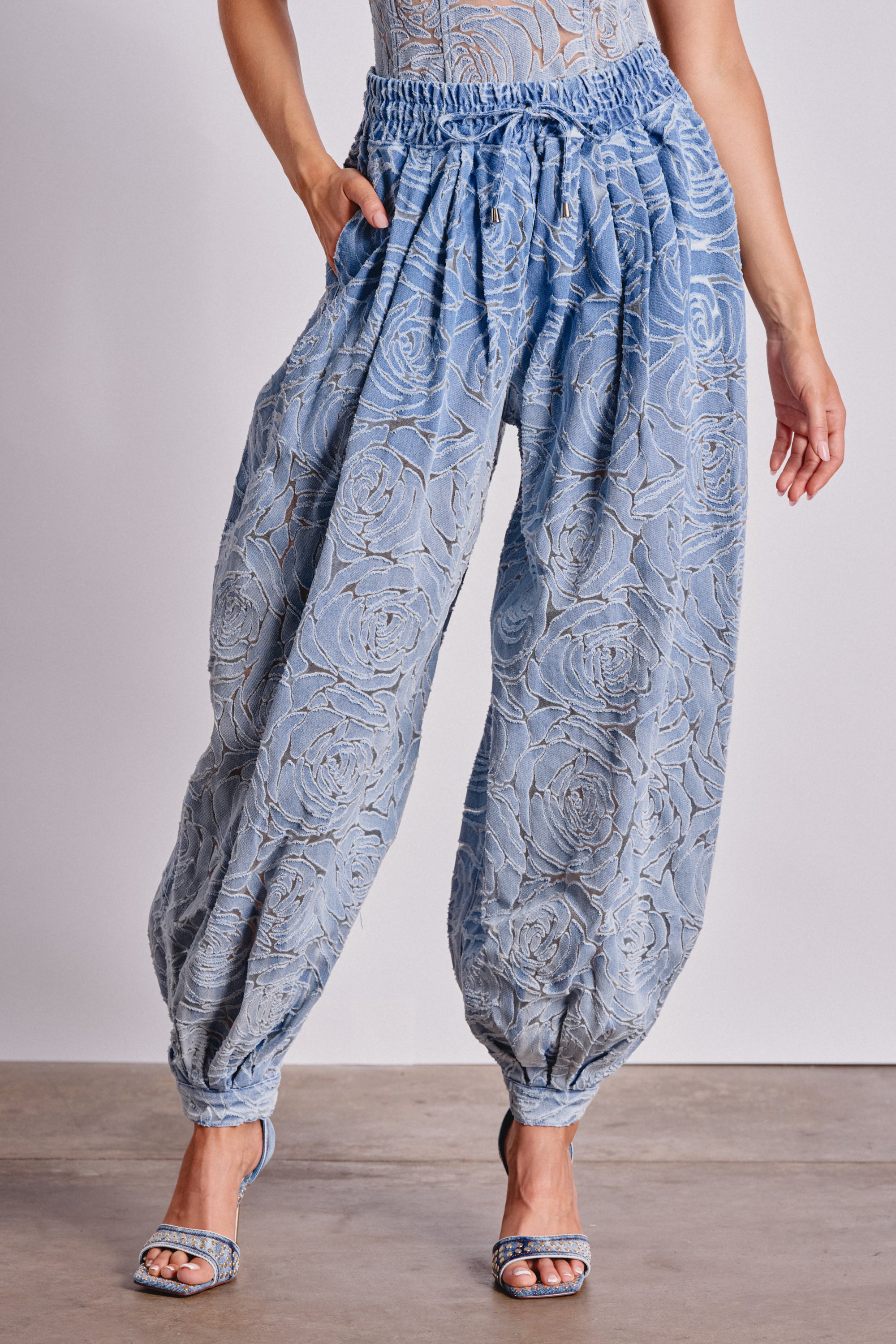 Wearing the DENIM FOR DAYS BALLOON PANT in a high-rise light blue floral denim with gathered waist and ankles, styled with matching heeled sandals and a semi-sheer top. 1