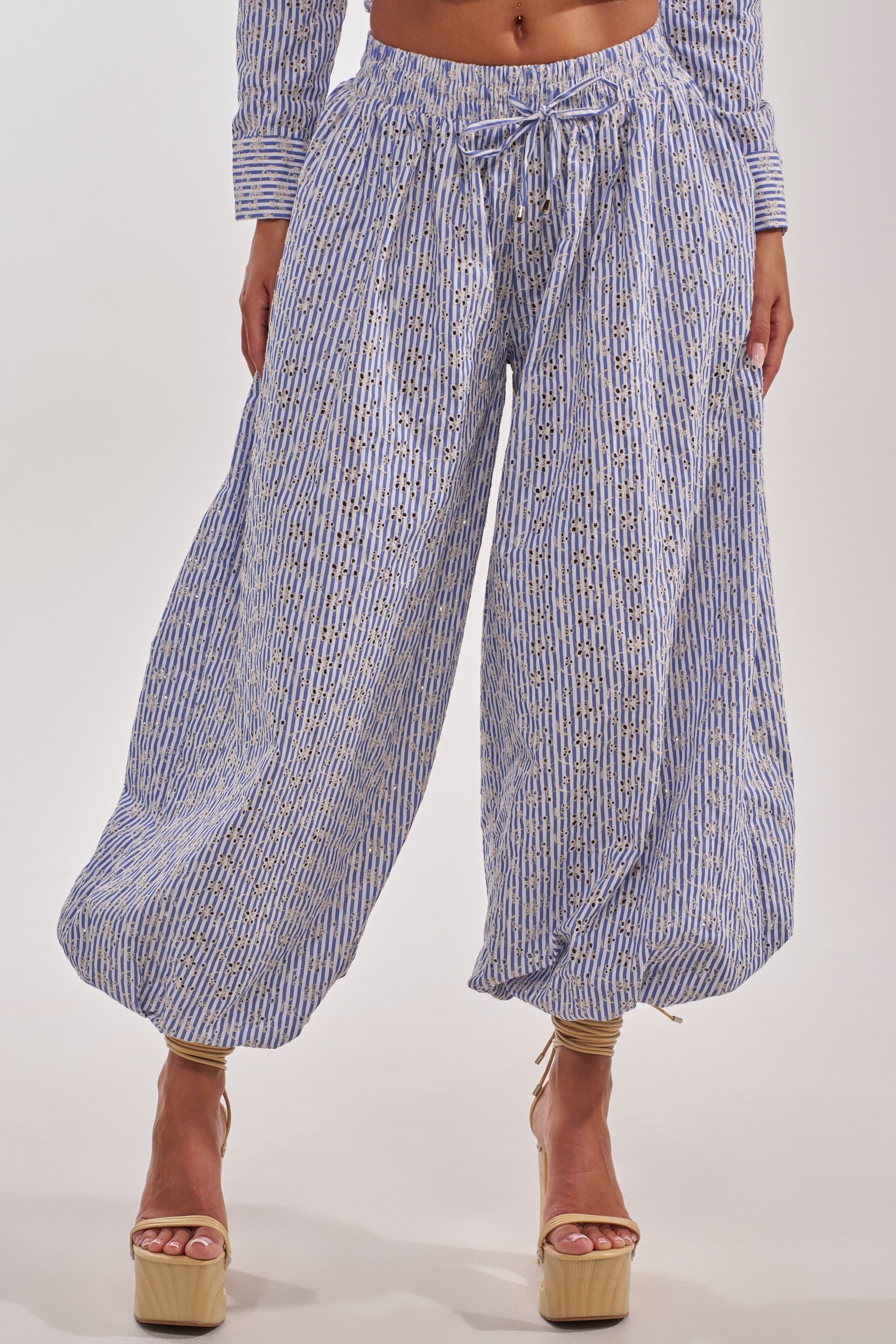 A person wears BLOSSOM BALLOON PANT, featuring a high-waisted, wide-leg silhouette in blue and white patterns, paired with beige platform heels. The cropped photo (shoulders to feet) is set against a white background. 4