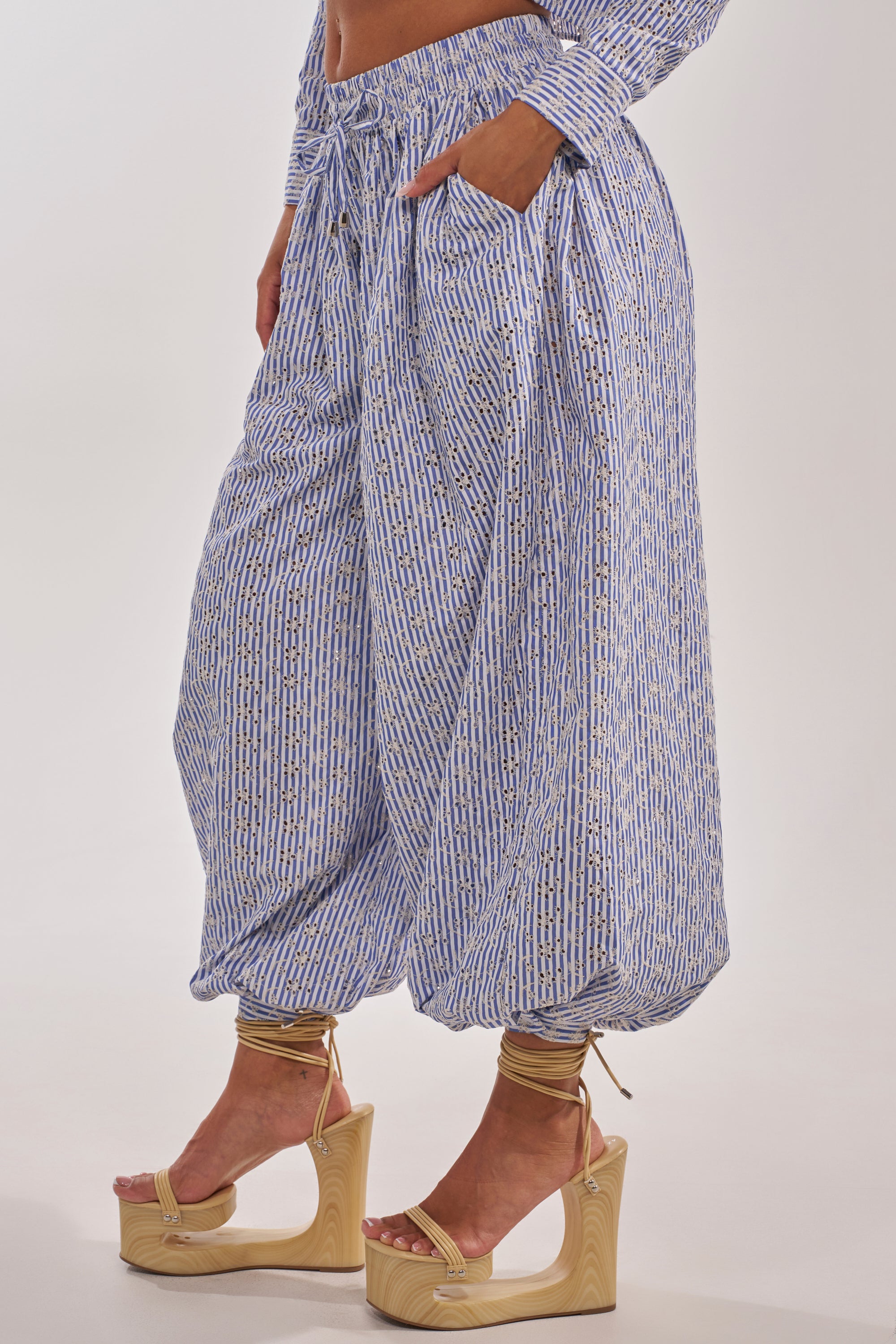 Someone wearing the BLOSSOM BALLOON PANT, a loose, blue-and-white patterned high-waisted style with pockets, paired with strappy beige platform sandals against a plain background. 5