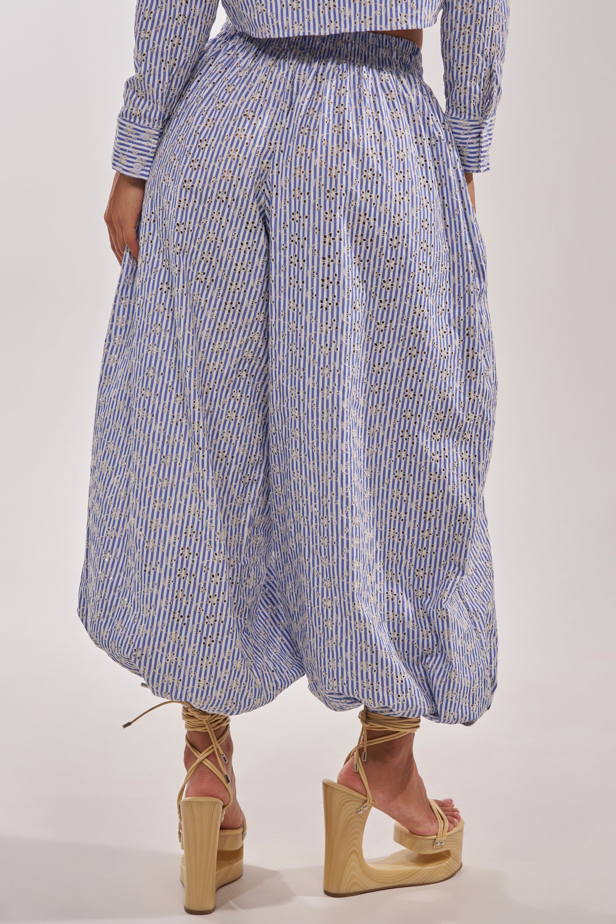 A person wears the BLOSSOM BALLOON PANT in loose blue and white stripes with a high waist and elastic waistband, paired with strappy wooden platform heels. The rear view highlights the wide-leg, balloon silhouette of the pants. 6
