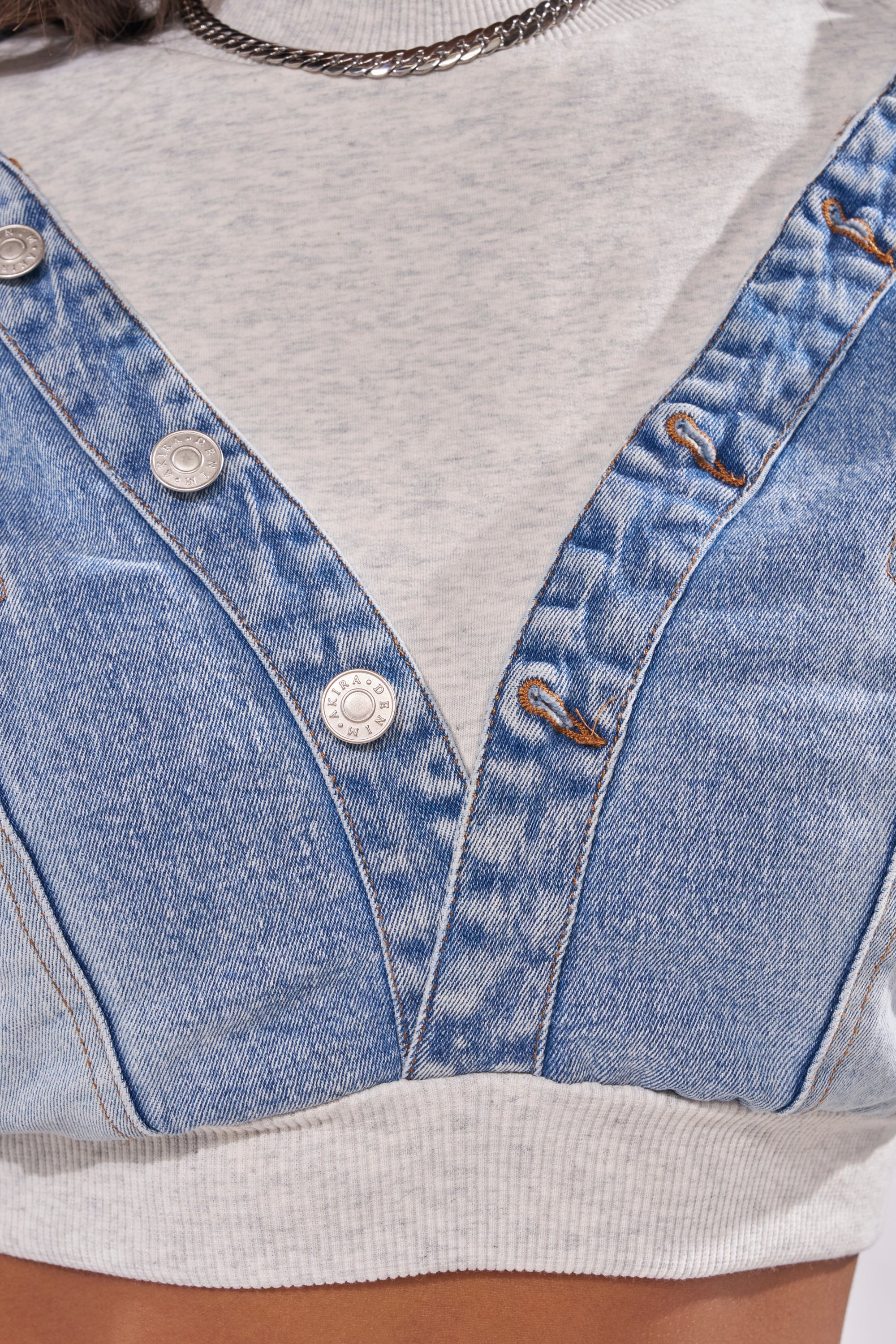 Close-up of a person wearing the DOUBLE FUN SWEATSHIRT—a light gray top with denim overall-style accents, silver buttons, and brown stitching details. A silver chain necklace peeks out at the neckline for a chic street-style vibe. 6