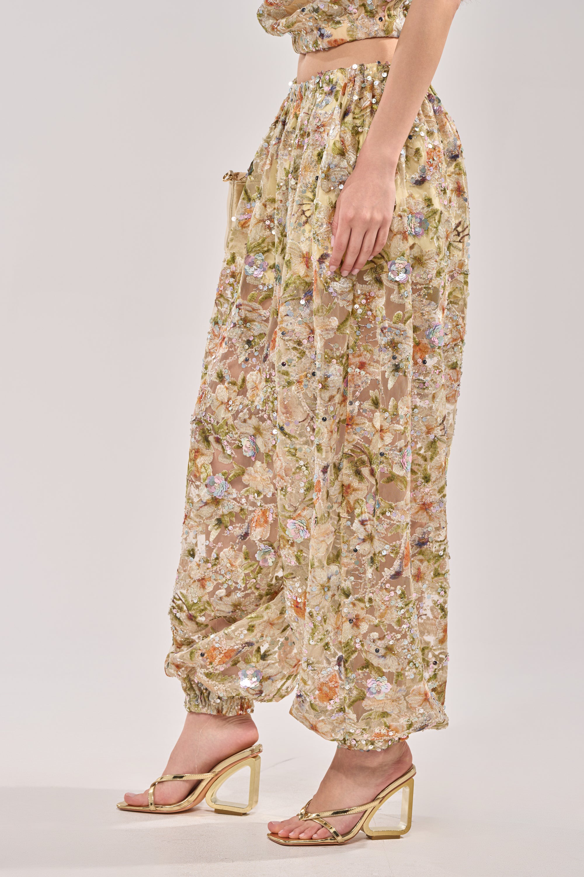 A person models the LETS TALK ABOUT IT BALLOON PANT in beige sheer fabric with floral embroidery, paired with strappy gold block-heeled sandals, standing against a plain light background. 3
