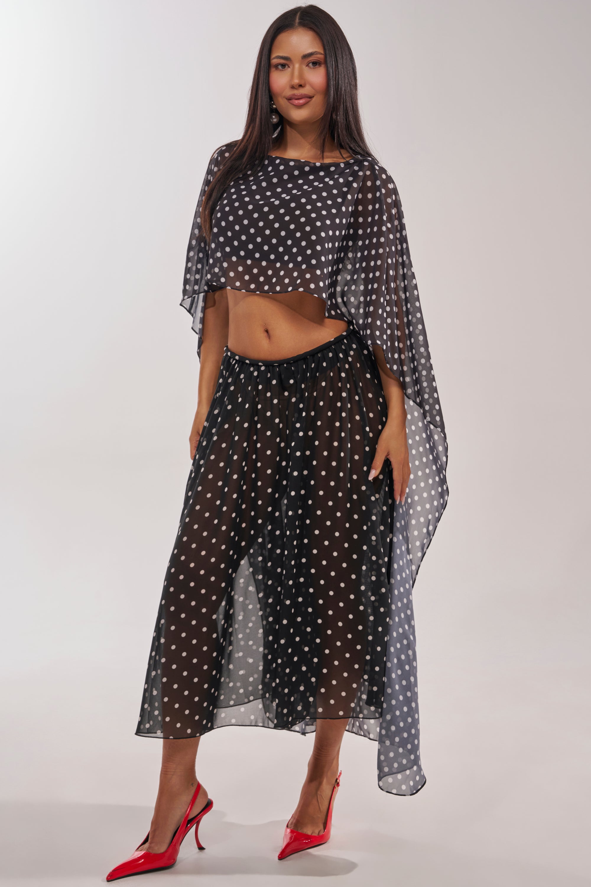A woman models the COOL GIRL POLKA DOT GAUCHO PANT—black, sheer, flowy polka dot pants with a matching top—paired with bright red heels, set against a plain light background. 6