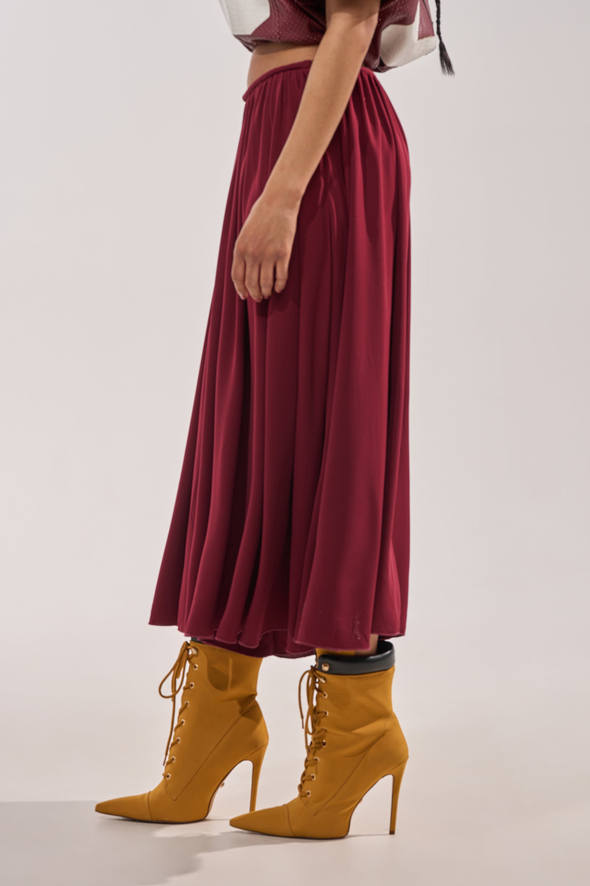 A person stands sideways against a plain light background wearing the COOL GIRL GAUCHO PANT in wine with a wide-leg, high-rise fit, paired with mustard yellow lace-up heeled boots. 4