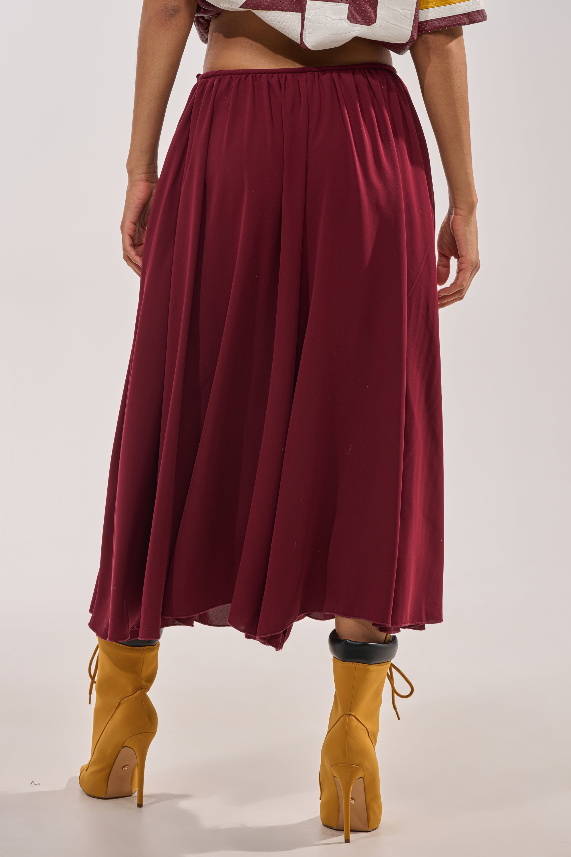 Person is standing on a light background, photographed from behind, wearing the COOL GIRL GAUCHO PANT in maroon with a wide-leg silhouette and yellow high-heeled ankle boots, showcasing the back view from waist to feet. 5