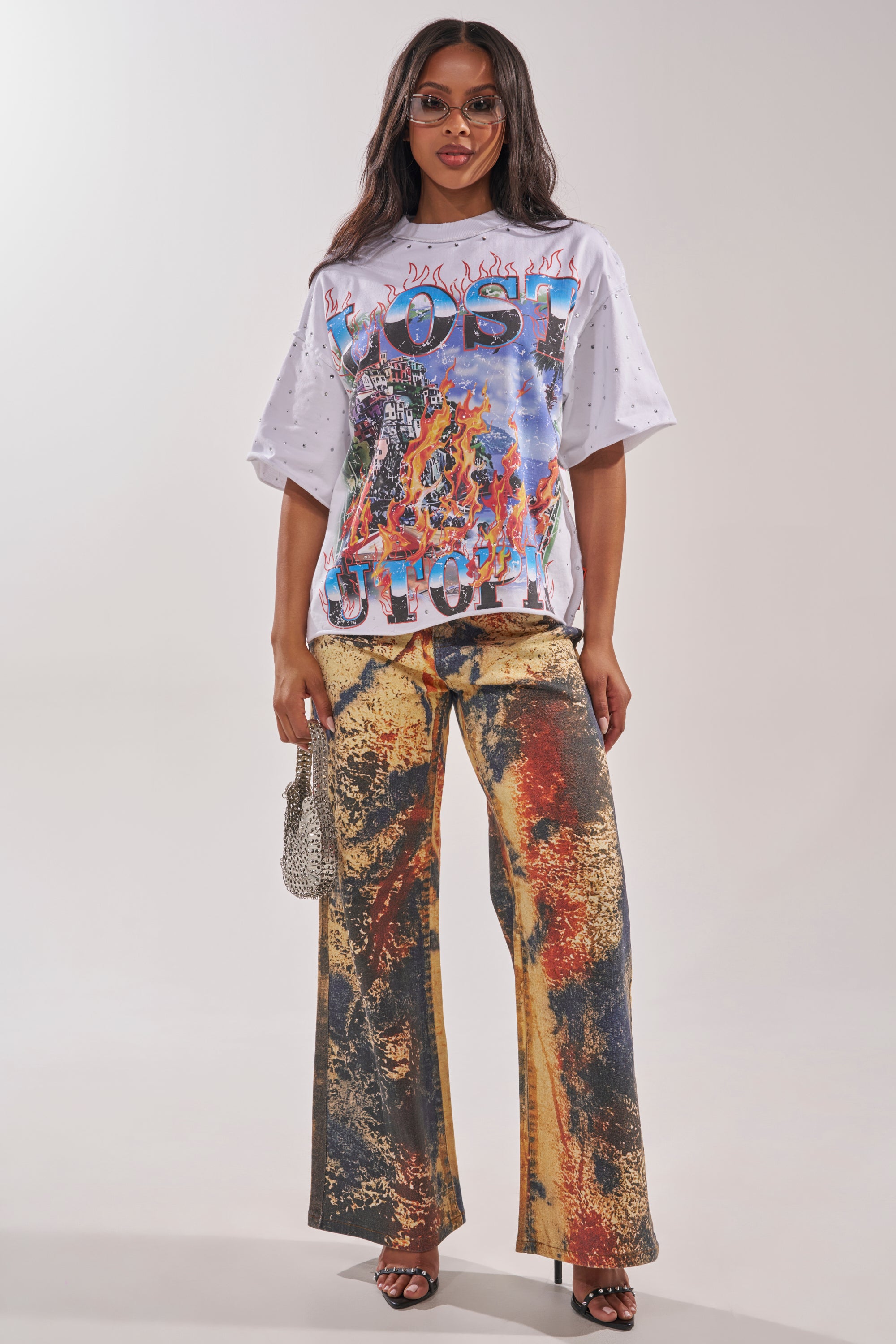 A woman wearing sunglasses, a graphic "LOST FUTURE" tee with flames and colorful designs, POWER SQUAD RELAXED DENIM in earthy tones, black sandals, and holding a small silver handbag. 4
