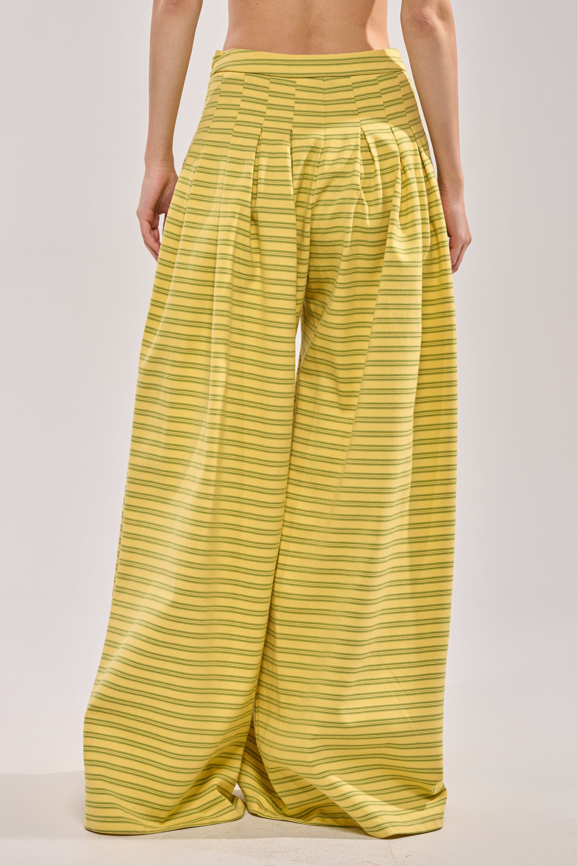 Person seen from behind wearing SILVER COAST YELLOW STRIPE TROUSER—wide-leg summer pants in yellow with thin green horizontal stripes, set against a plain light background. 2