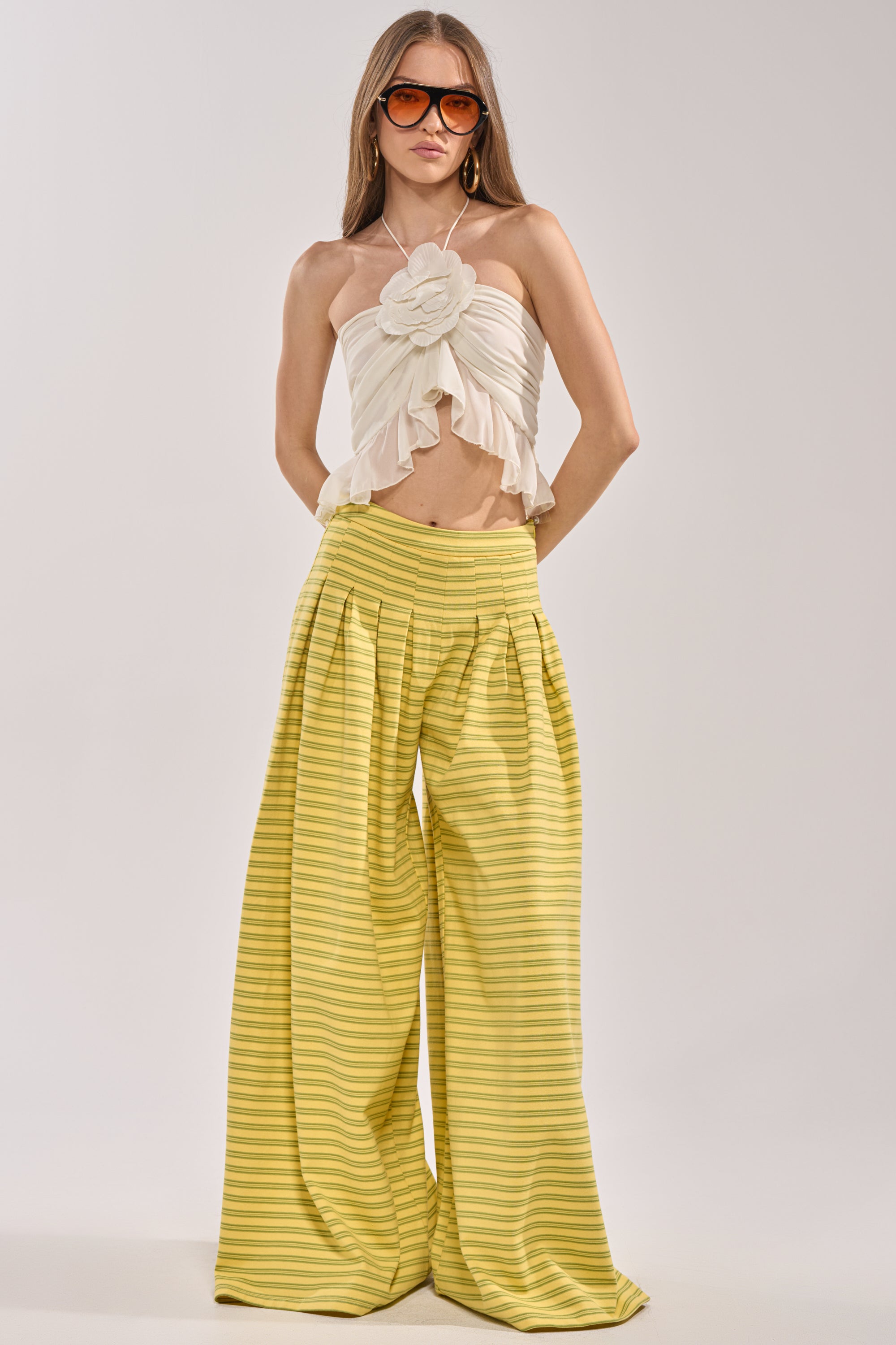 A woman wearing oversized sunglasses, a strapless white ruffled top with a flower detail, and the SILVER COAST YELLOW STRIPE TROUSER stands against a plain background. 4