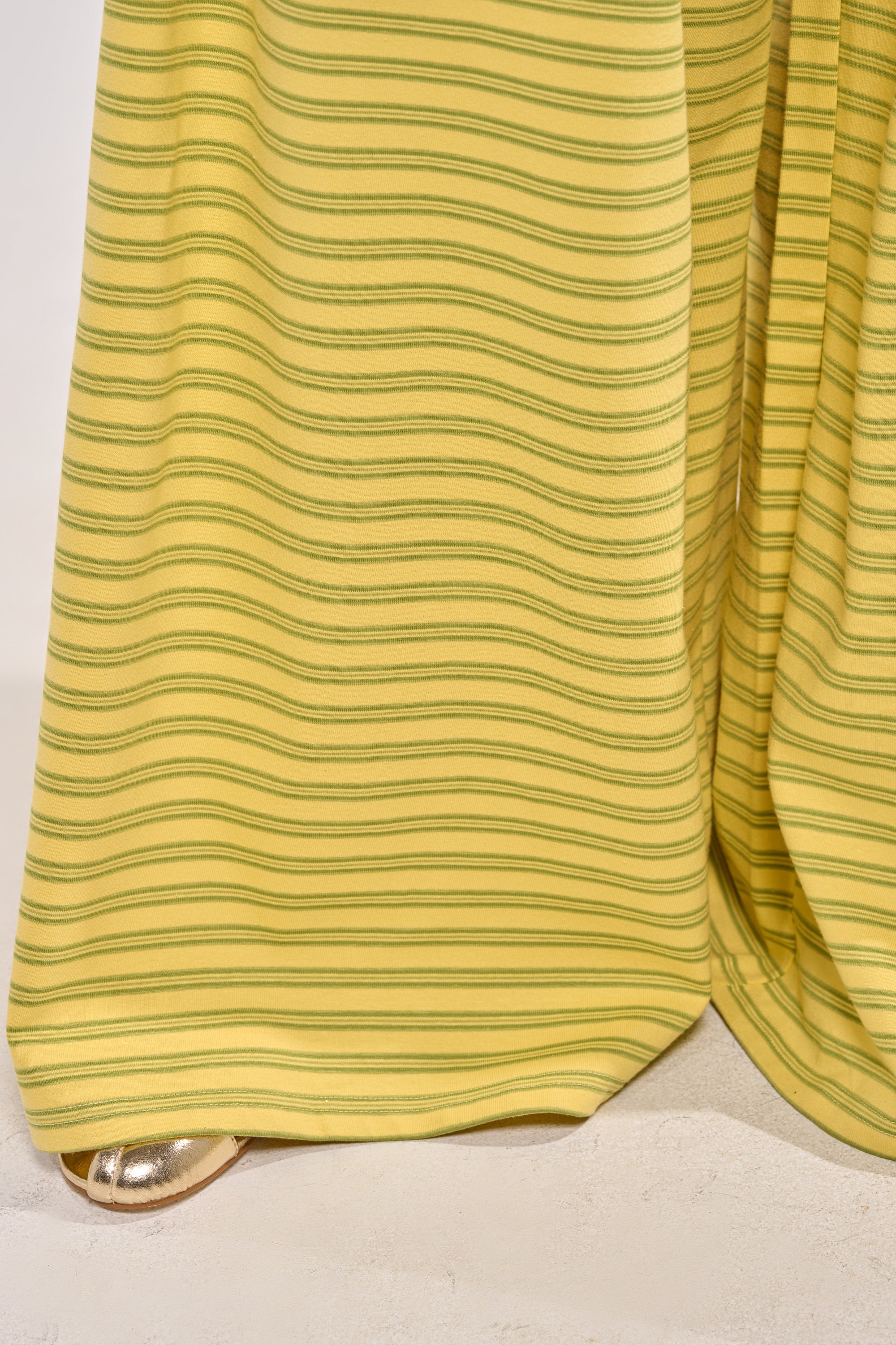 A close-up of the SILVER COAST YELLOW STRIPE TROUSER, featuring wide-leg yellow cotton with green stripes over a metallic gold shoe against a light background—ideal for summer style. 5