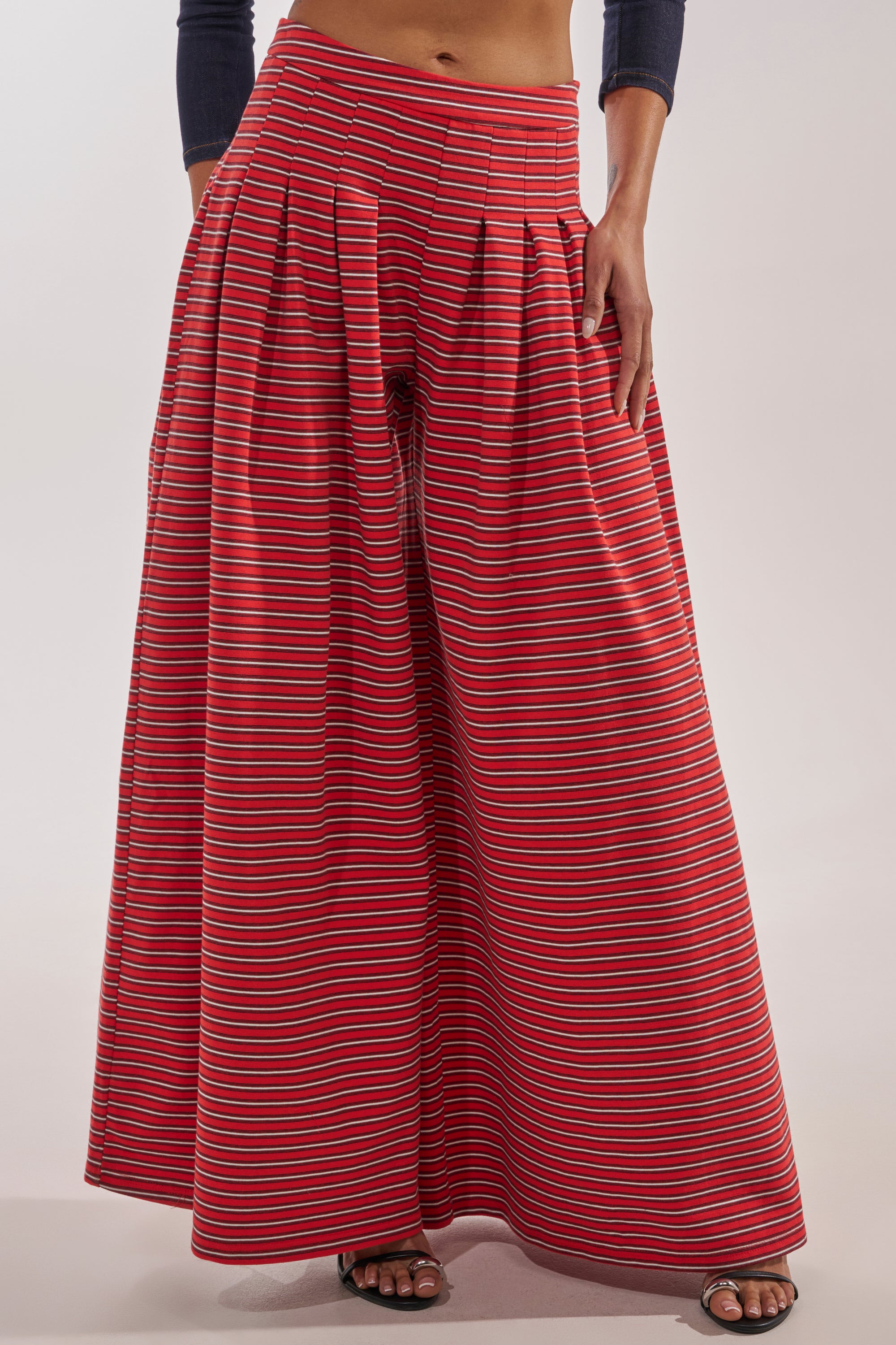Only the lower half of a person is visible, wearing the SILVER COAST STRIPE TROUSER—cotton wide-leg pants with a high-rise waistband and horizontal multicolored stripes—paired with sandals. 1