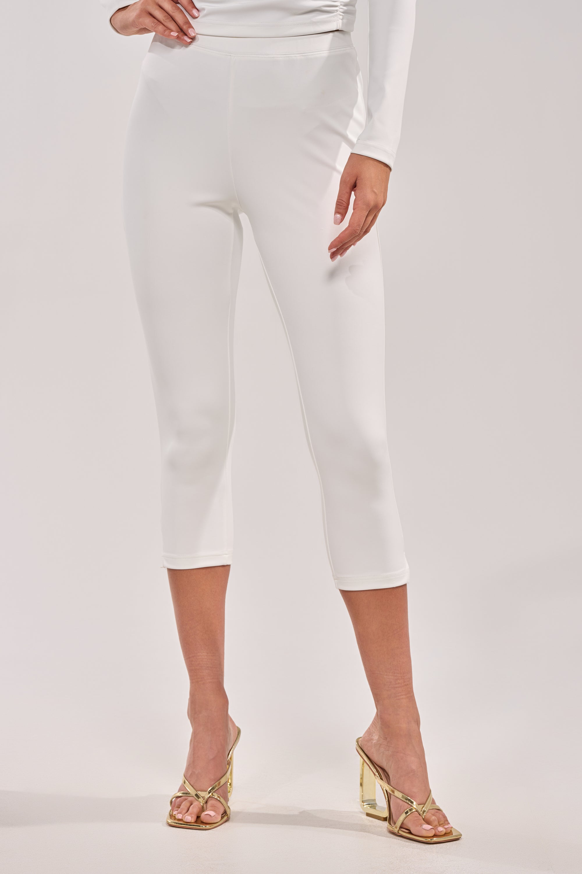 Wearing the MODEL OFF DUTY CAPRI and gold high-heeled sandals, a person stands against a plain light background with one hand on their hip.