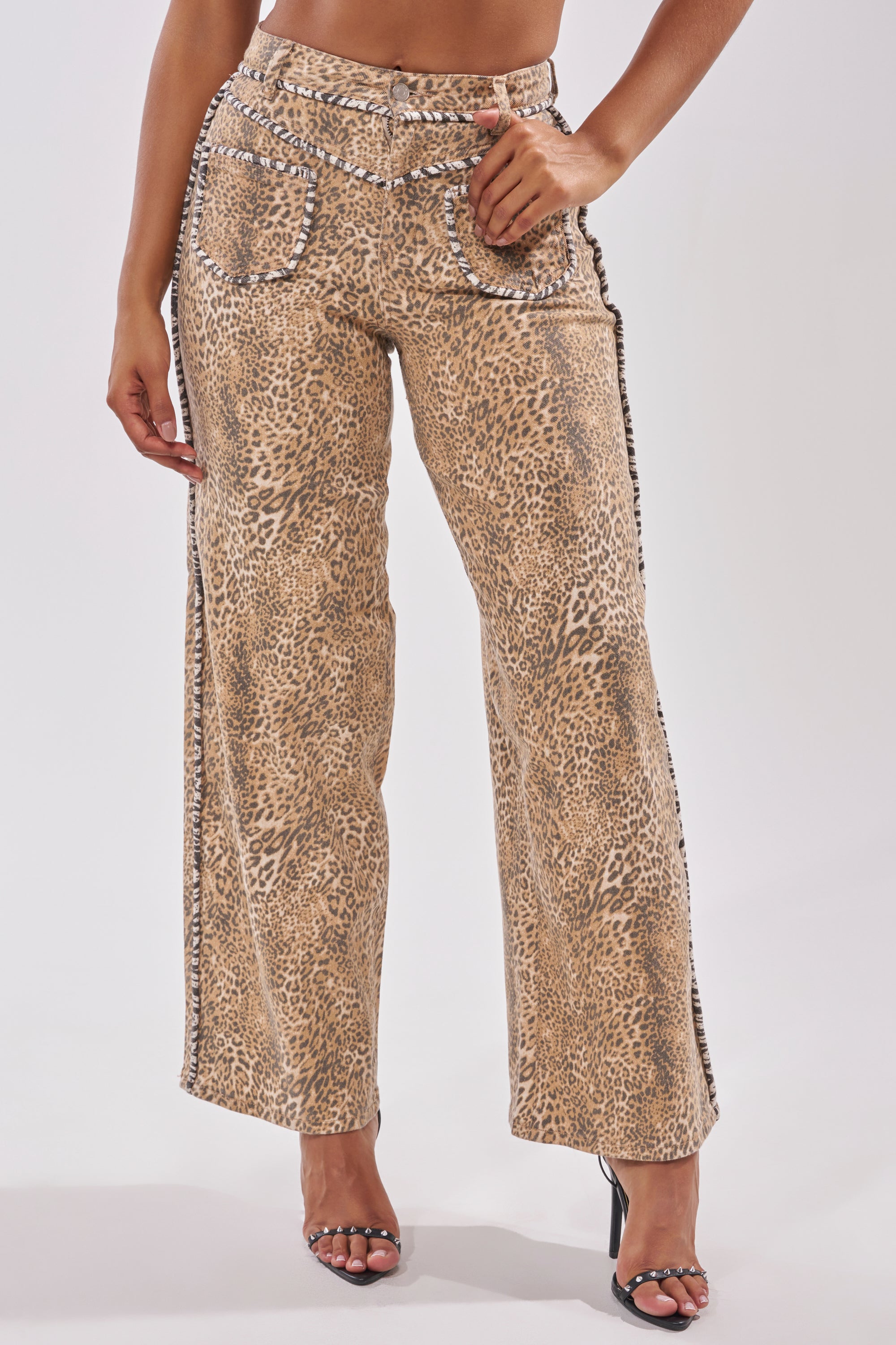 Wearing the IN THE WILD LEOPARD DENIM—high-waisted, wide-leg leopard print pants with studded pocket and side seam details—paired with black open-toe heels. Only the lower half is visible. 1