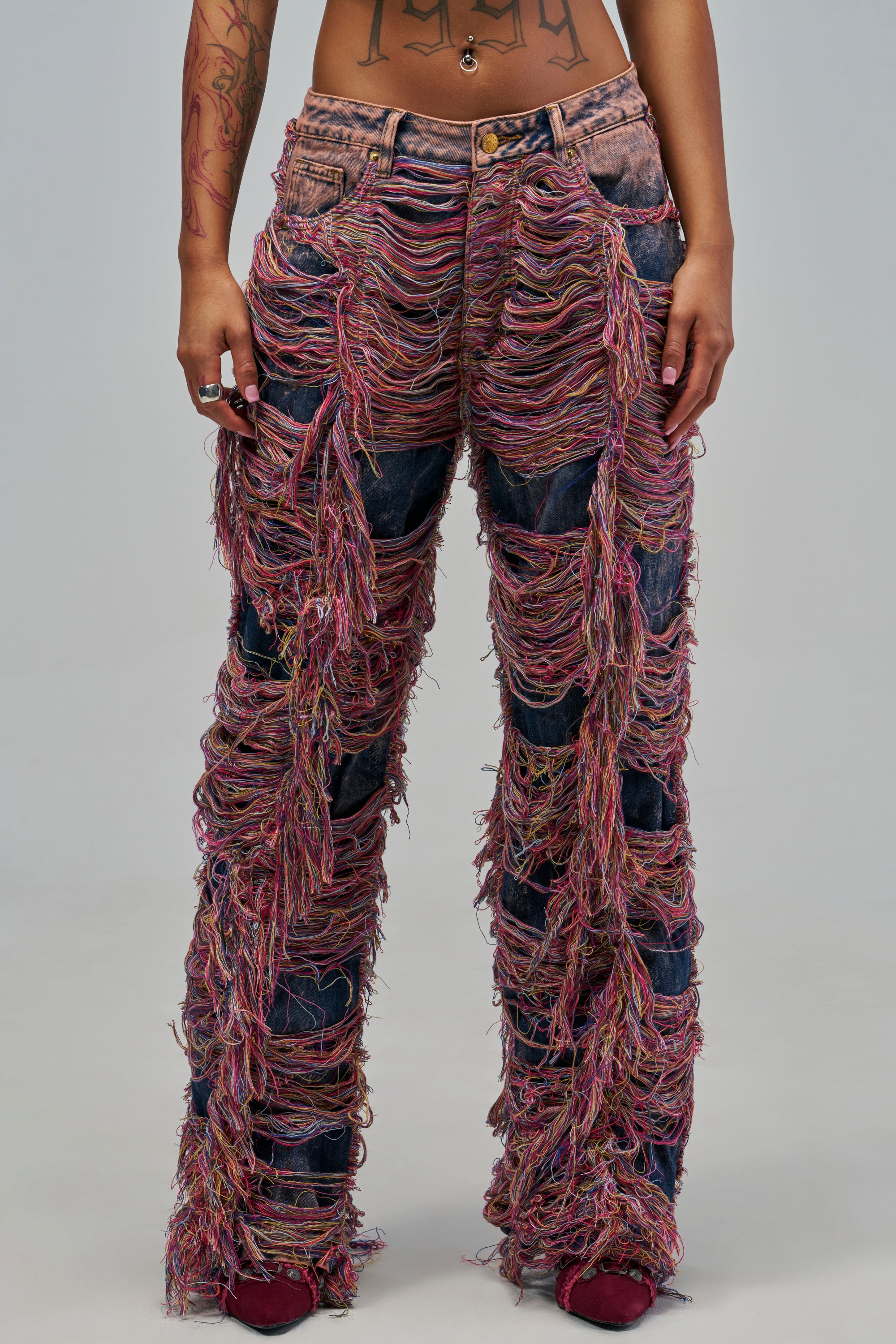 ON TOP OVERLY DISTRESSED RELAXED DENIM low-rise, acid wash jeans featuring heavy distressing and long, multicolored frayed threads covering the legs for a festival-inspired look.