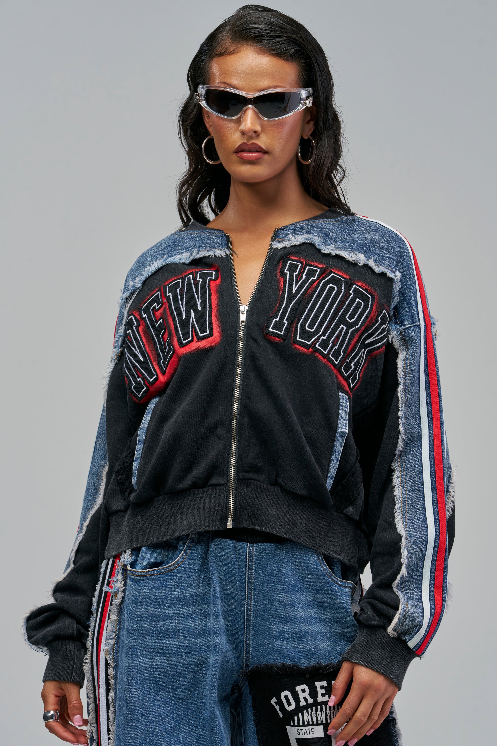 A person wearing a black CHAMPION ZIP UP SWEATSHIRT with “NEW YORK” embroidered on the front, featuring denim shoulder and sleeve accents with red and white stripes.