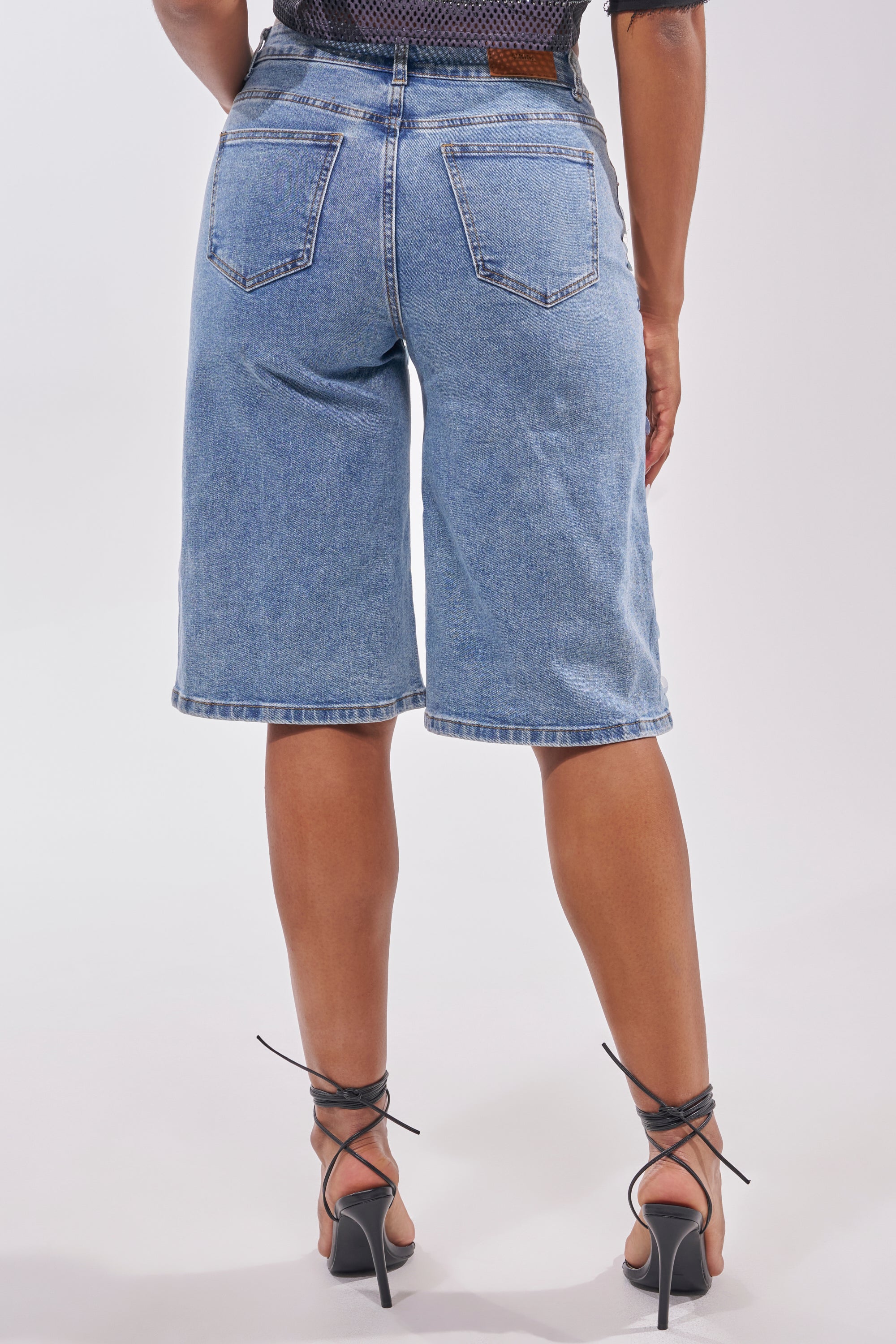 A person wearing SPARKLE AND SHINE BERMUDA SHORTS and black strappy high-heeled sandals, shown from the back against a plain white background—perfect for festivals and standout statement looks. 4