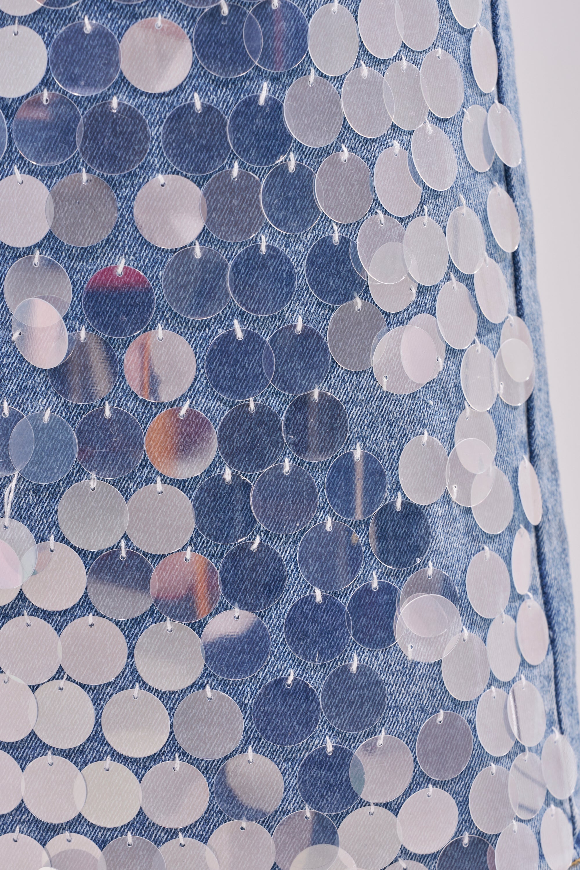 Close-up of blue denim fabric adorned with shiny round silver sequins, perfect for standout festival style—just like the SPARKLE AND SHINE BERMUDA SHORT featured in this collection. 6