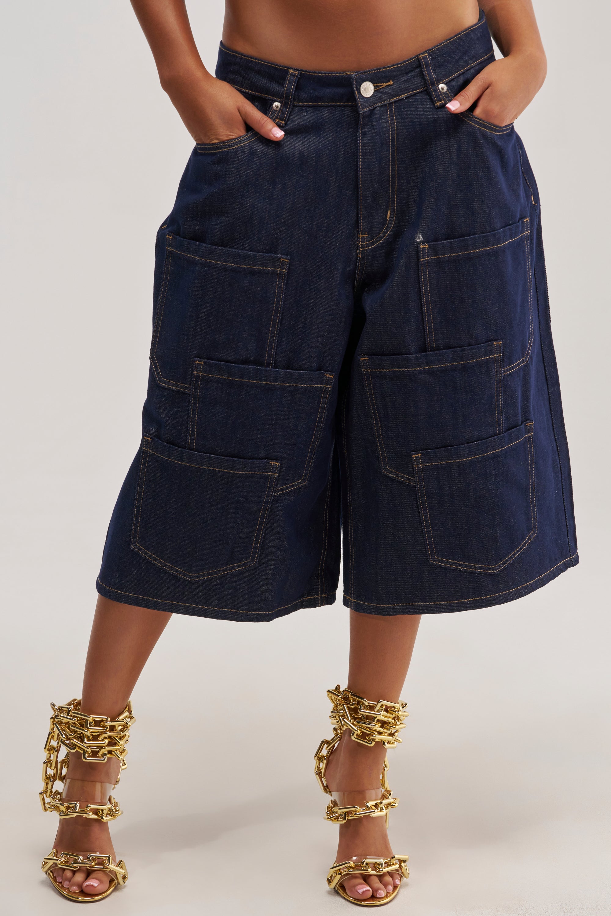 Wearing the POCKETS ALL OVER DENIM CULOTTE, a person stands against a neutral background, showcasing effortless streetwear style with dark-wash denim and bold, functional front pockets.
