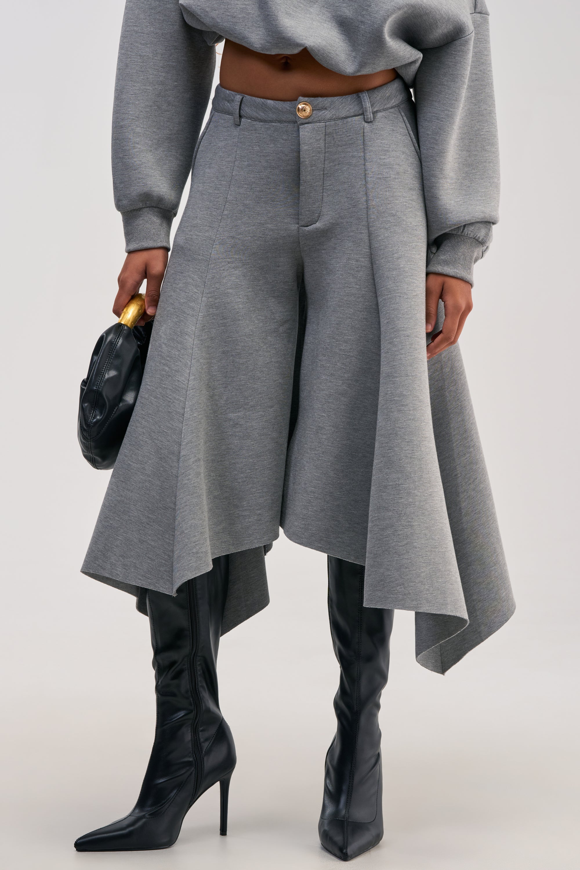 Person wearing WILD AND FREE CULOTTES in grey with a wide, draped silhouette and high-rise waistband, paired with a matching cropped sweatshirt and black high-heeled boots, holding a black clutch. Only the outfit is visible from mid-torso down.