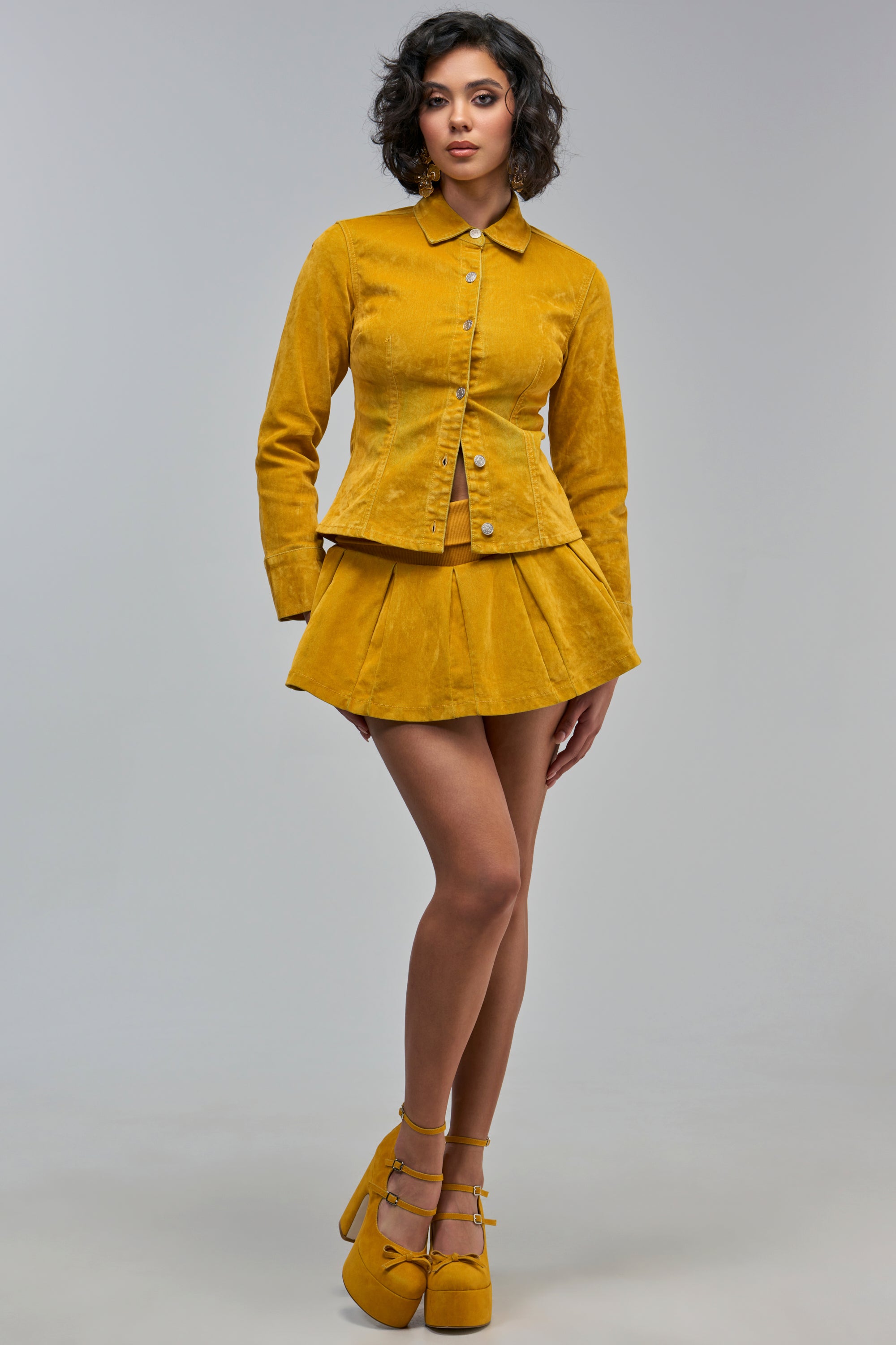 A person wearing a mustard yellow button-up jacket and a matching GOLDEN GIRL VELVET DENIM MINI SKIRT, paired with yellow platform heels for fall styling.