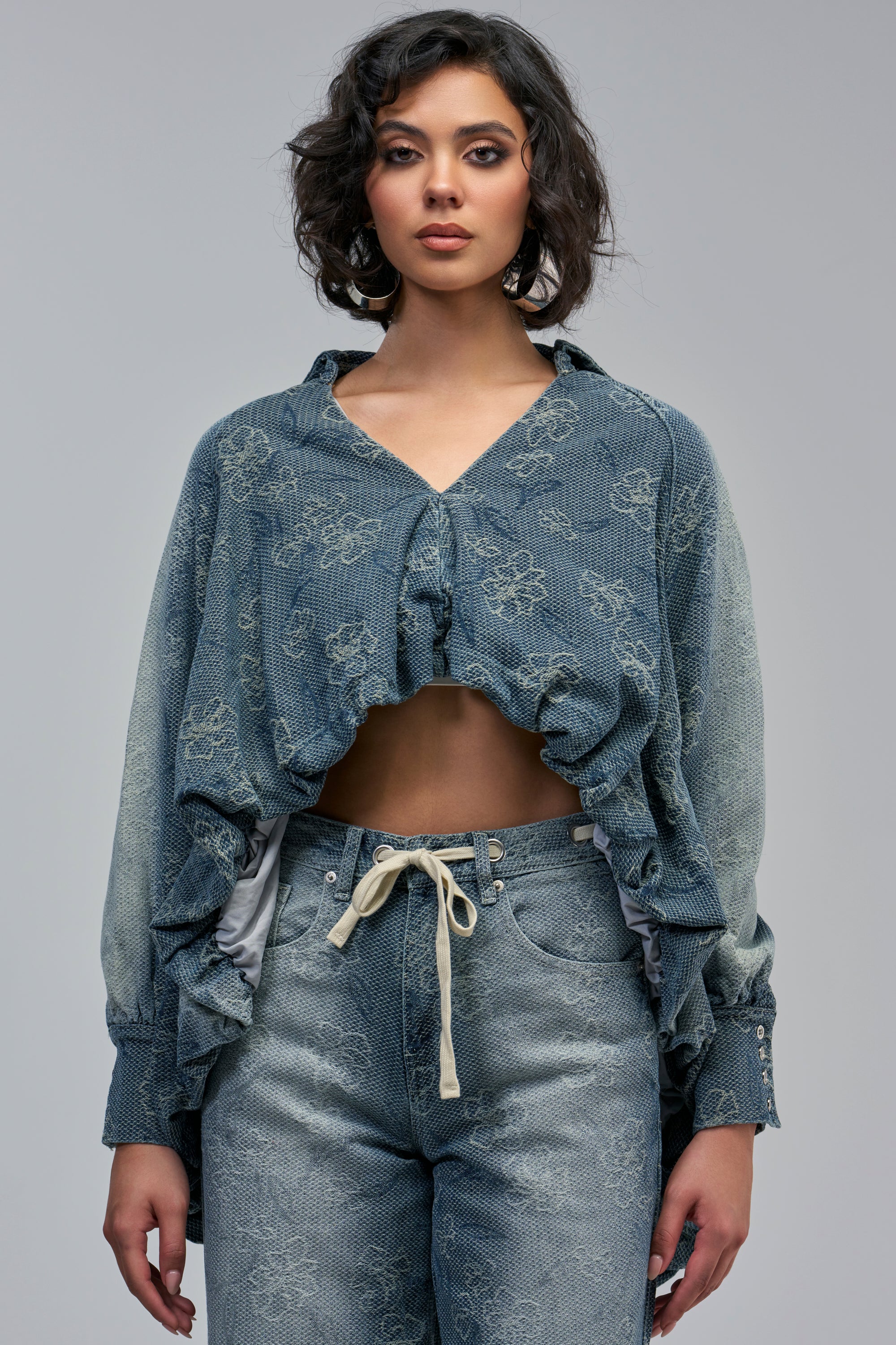 ALICE EMBROIDERED DENIM BLOUSE, a cropped, light wash denim blouse featuring a floral pattern and a draped front, worn with matching high-waisted jeans.