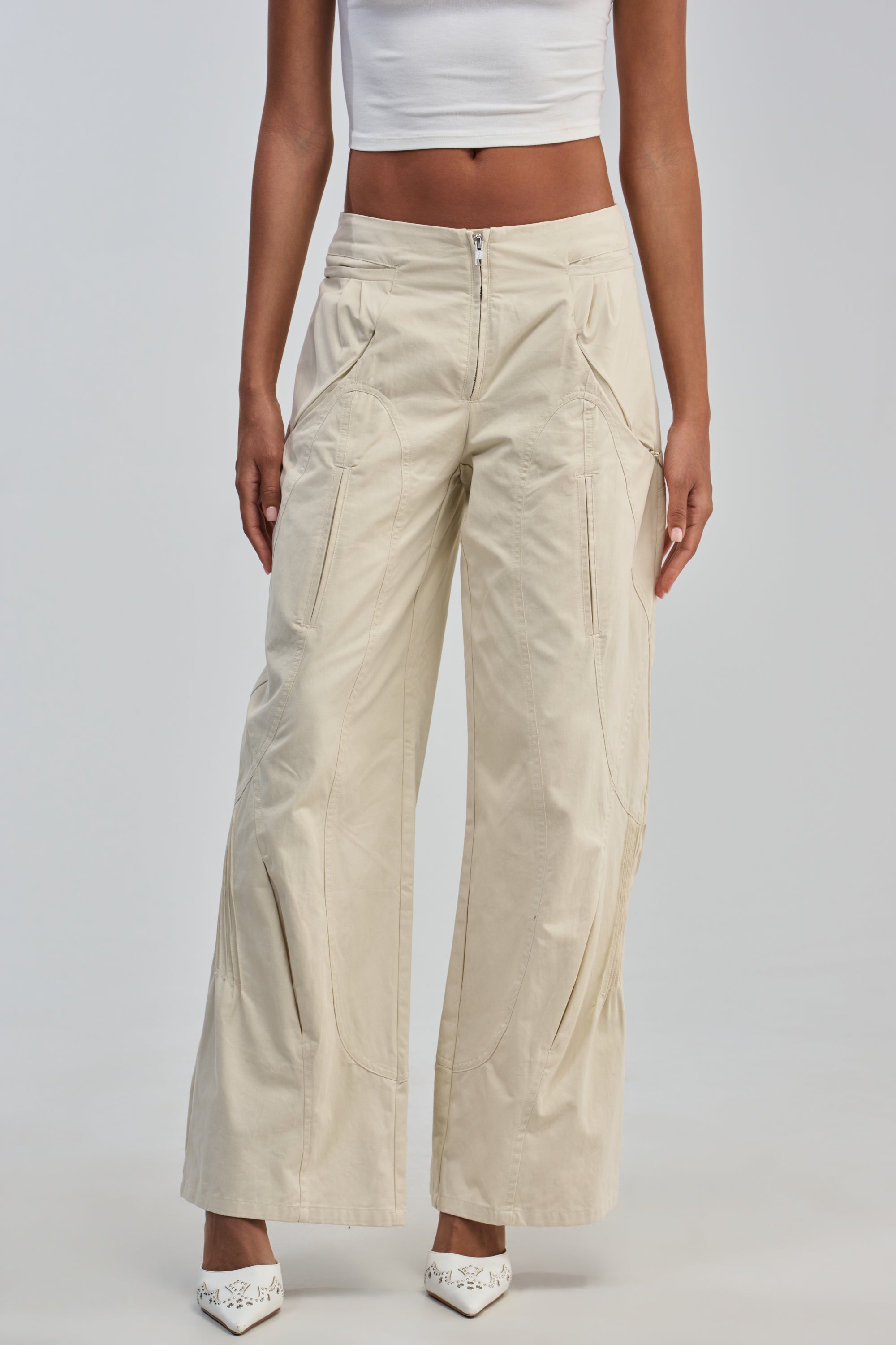 A person is wearing a white crop top, the LOW EFFORT HIGH IMPACT PANTS—ivory cargo pants with multiple pockets in a streetwear style—and white shoes, standing against a plain light background.