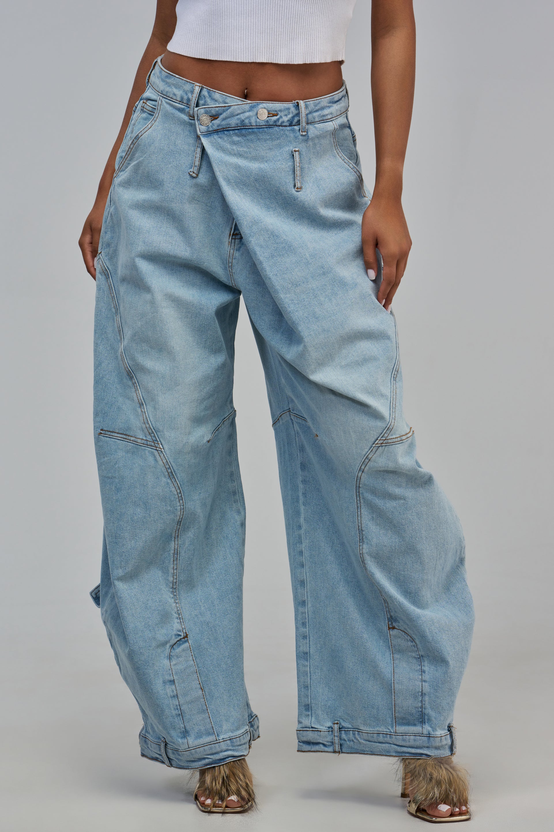 IZZY RELAXED DENIM LIGHT BLUE jeans in a light wash with a relaxed barrel silhouette, featuring an asymmetrical crossover waistband and prominent stitched panel detailing.