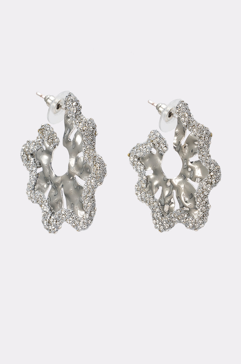 Meet the TOO WAVY EARRING: silver wavy hoops with an irregular, textured design, encrusted with small clear rhinestones. These statement earrings feature posts with clear backings for a stylish finishing touch.