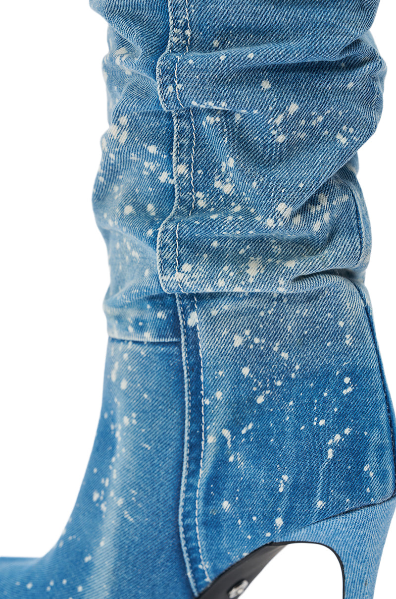 The AZALEA WANG JEANNI DENIM SPLATTER PAINTED STILETTO BOOT features blue denim with white paint splatter, visible stitching, a chunky heel, and a scrunched ankle for a textured, relaxed look.