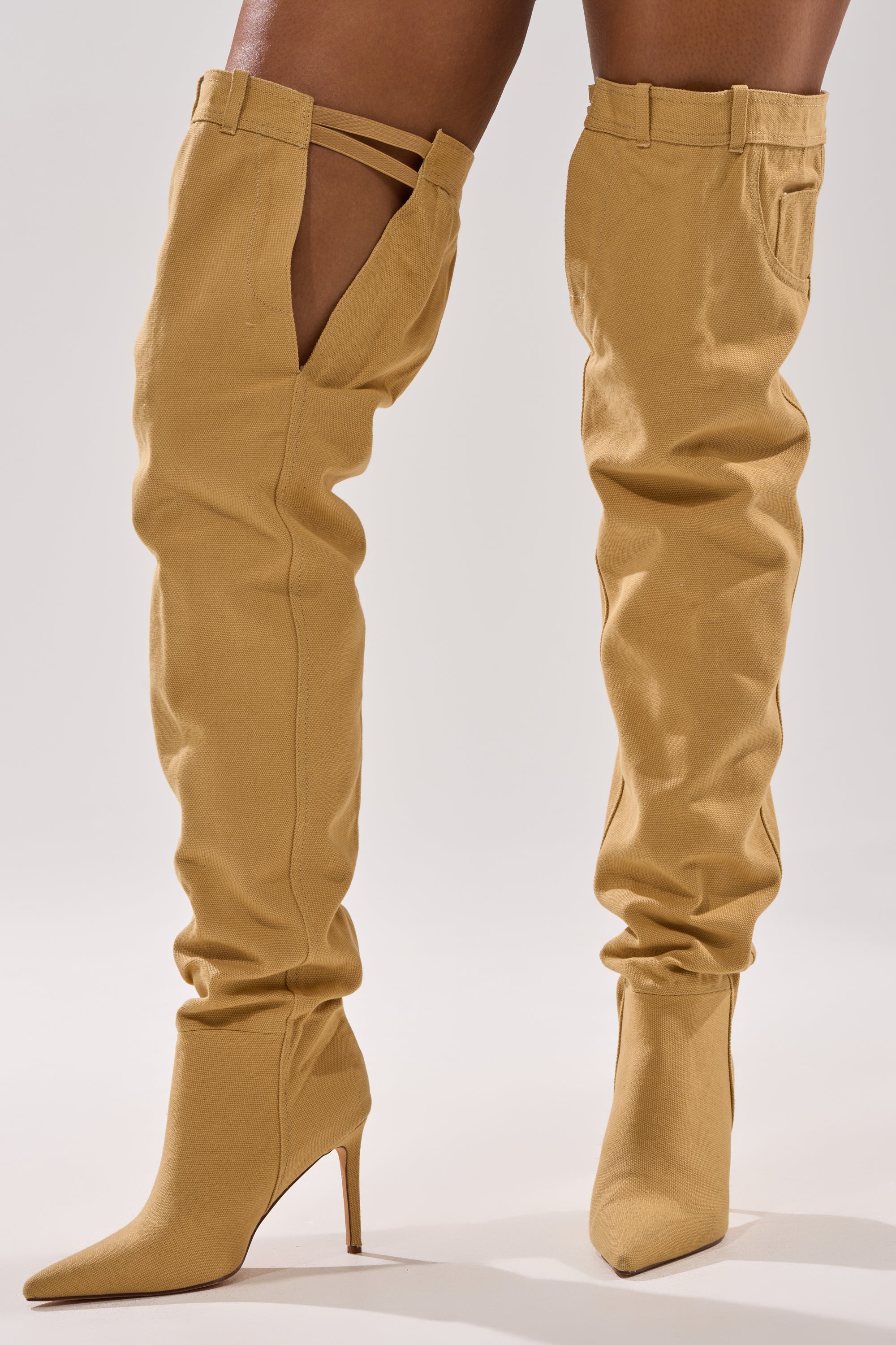 A person wears the AZALEA WANG JEANNI TAN PANT DETAIL OVER THE KNEE BOOT, featuring a slouchy fit, pointed toes, stylish top cutout details, and a high stiletto heel.
