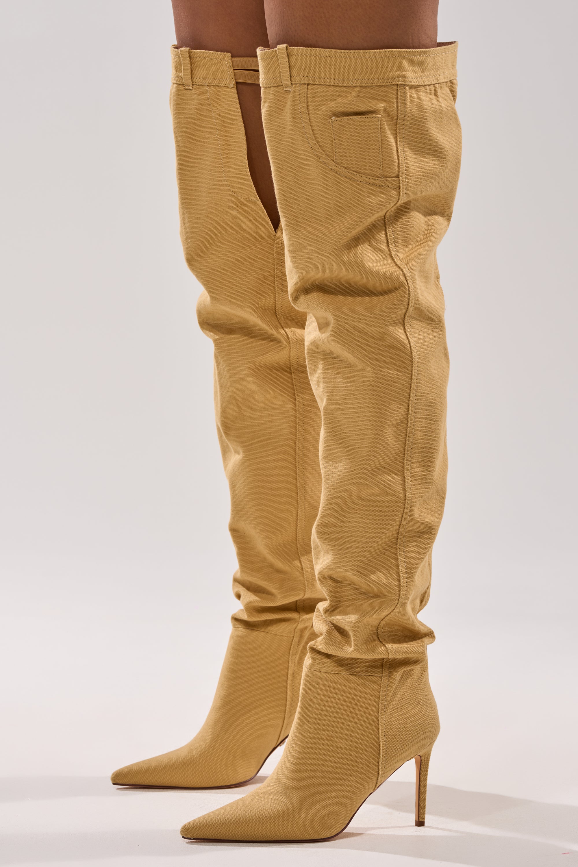 A person models the AZALEA WANG JEANNI TAN PANT DETAIL OVER THE KNEE BOOT—denim thigh-highs with stiletto heels, pointed toes, and side pockets—standing against a plain light background.