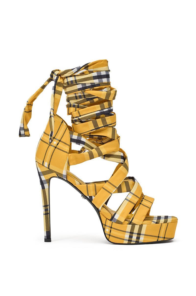 The AZALEA WANG JEMISHA YELLOW PLAID PLATFORM LACE UP SANDAL features a stiletto heel, multiple crisscross straps, and a wrap-around ankle tie, shown in a side profile view. 3