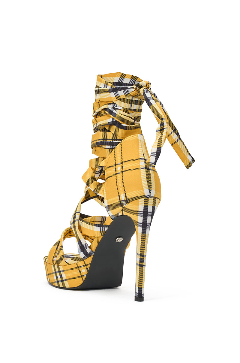The AZALEA WANG JEMISHA YELLOW PLAID PLATFORM LACE UP SANDAL features a yellow, black, and white plaid pattern, multiple crisscross straps, lace-up ankle detail, a thin stiletto heel, and a black sole. 5