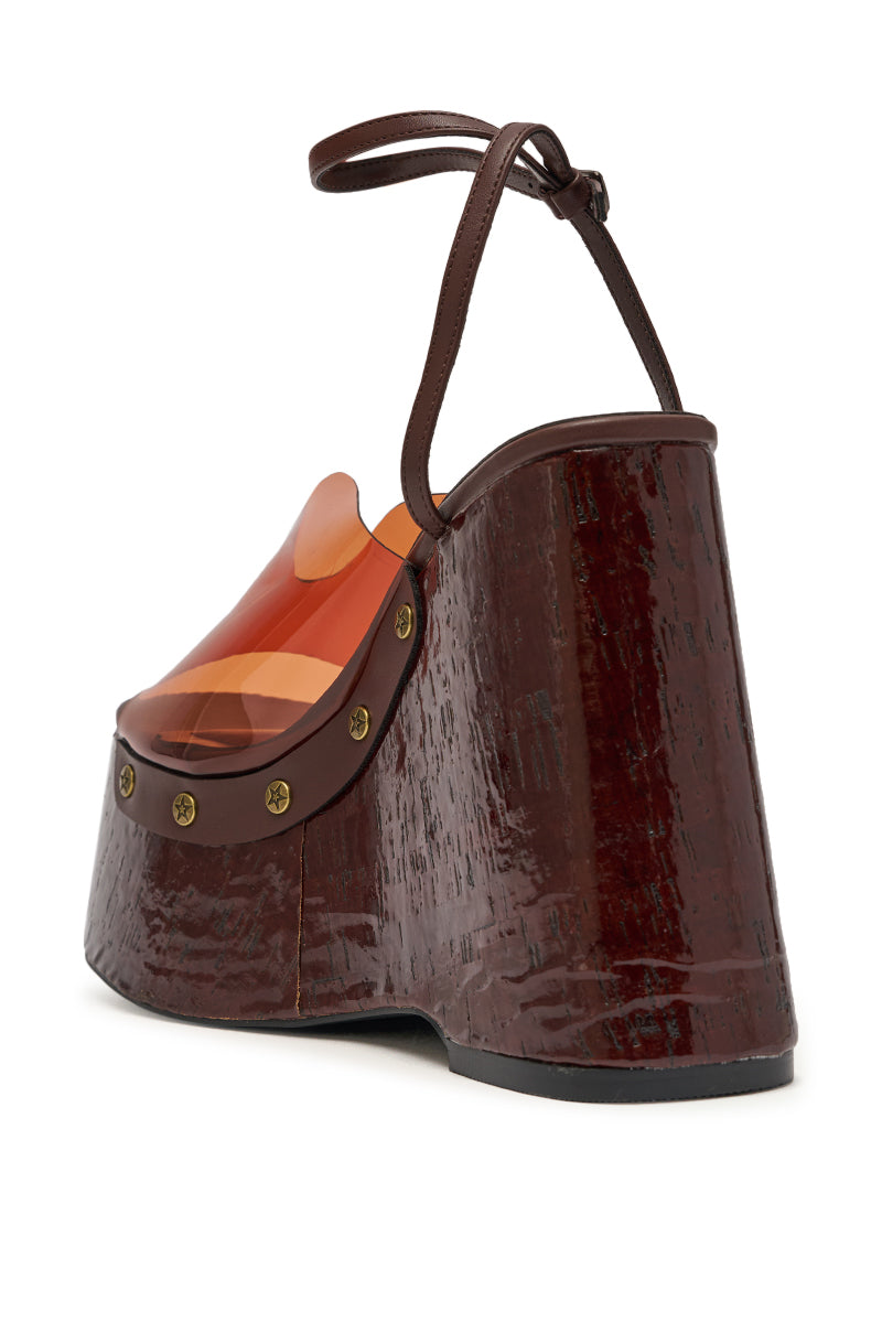 The AZALEA WANG JENZA CHOCOLATE WEDGE features a chunky dark brown wood-textured platform heel, brass studs, a translucent orange upper, and a thin brown ankle strap. 7