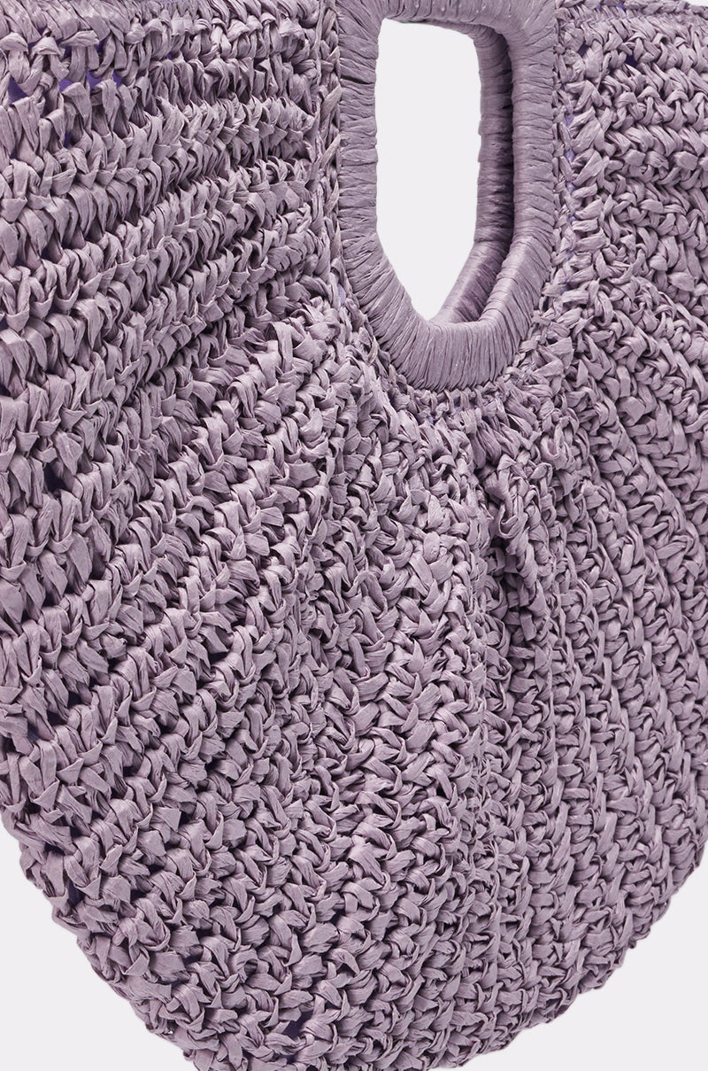 Close-up of the CATCHING FLIGHT RAFFIA CLUTCH, featuring a lavender woven raffia design with a round shape and square handle opening. The tightly woven fibers create a gathered effect for a unique boho-chic look. 3