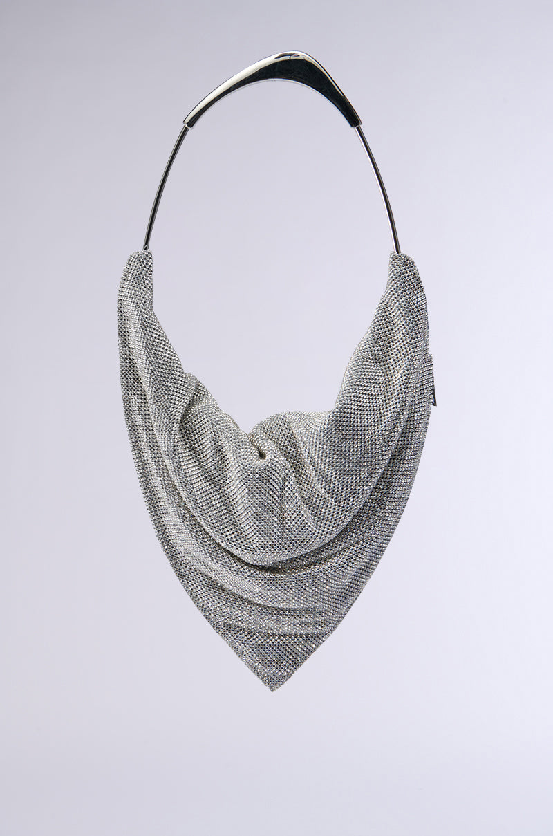 A luxurious IM IT LUXE RHINESTONE BAG is artfully displayed on a sleek, curved metal hanger against a plain background. The shimmering texture of the rhinestones exudes modern sophistication, echoing the elegant drape of a triangular metal mesh scarf. 0