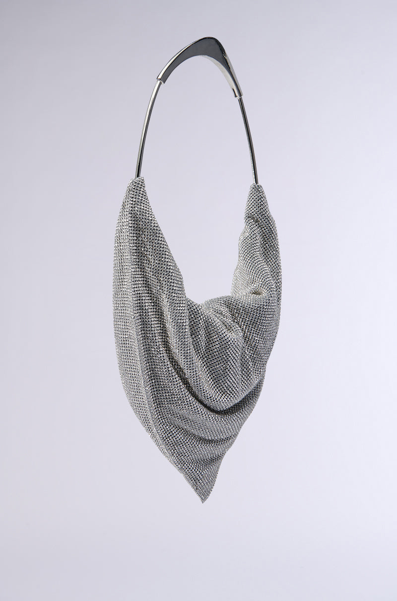Introducing the IM IT LUXE RHINESTONE BAG: This modern silver accessory features dazzling rhinestones and textured fabric elegantly draped over a curved metallic handle, set against a plain light gray background. 3